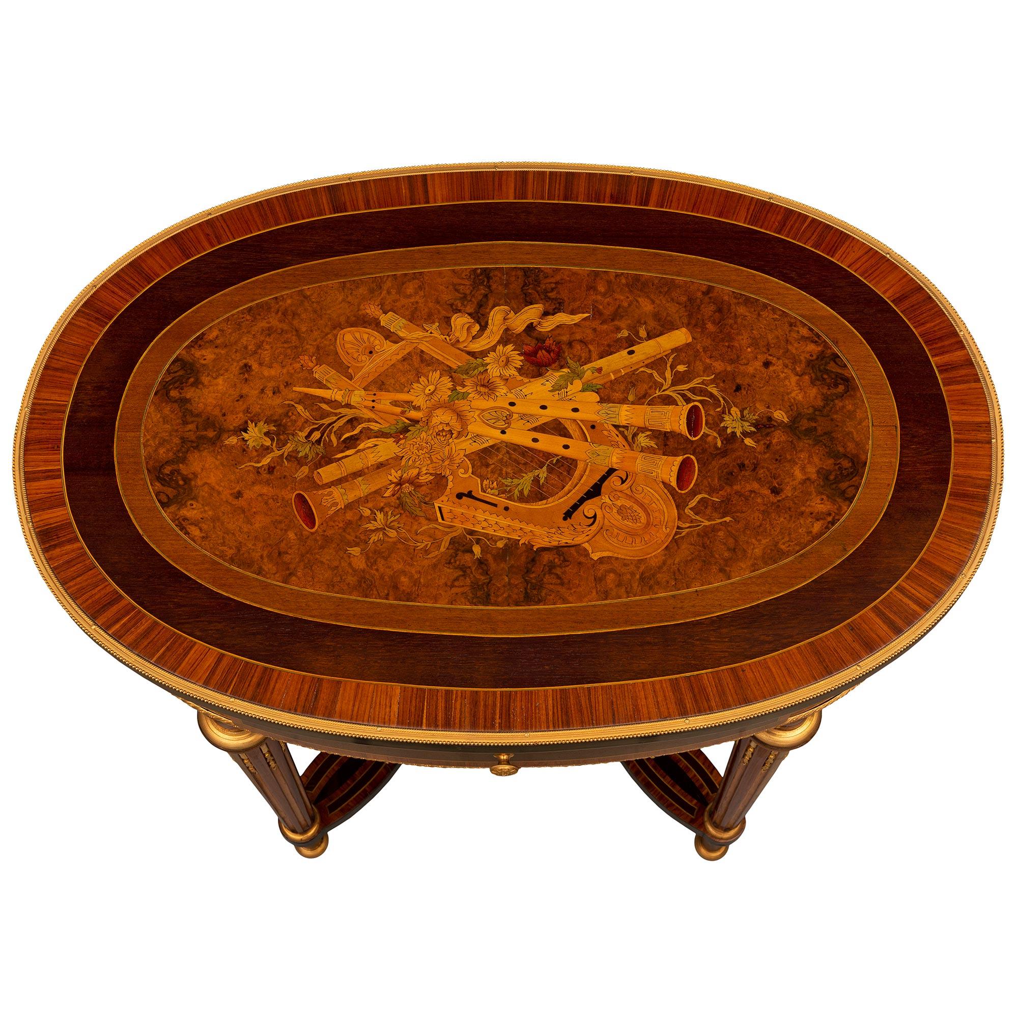 A striking French 19th century Louis XVI st. Kingwood, Tulipwood, burl Walnut and ormolu center table. The oval one drawer table is raised by elegant circular tapered fluted legs with fine mottled topie shaped feet and lovely fitted foliate ormolu