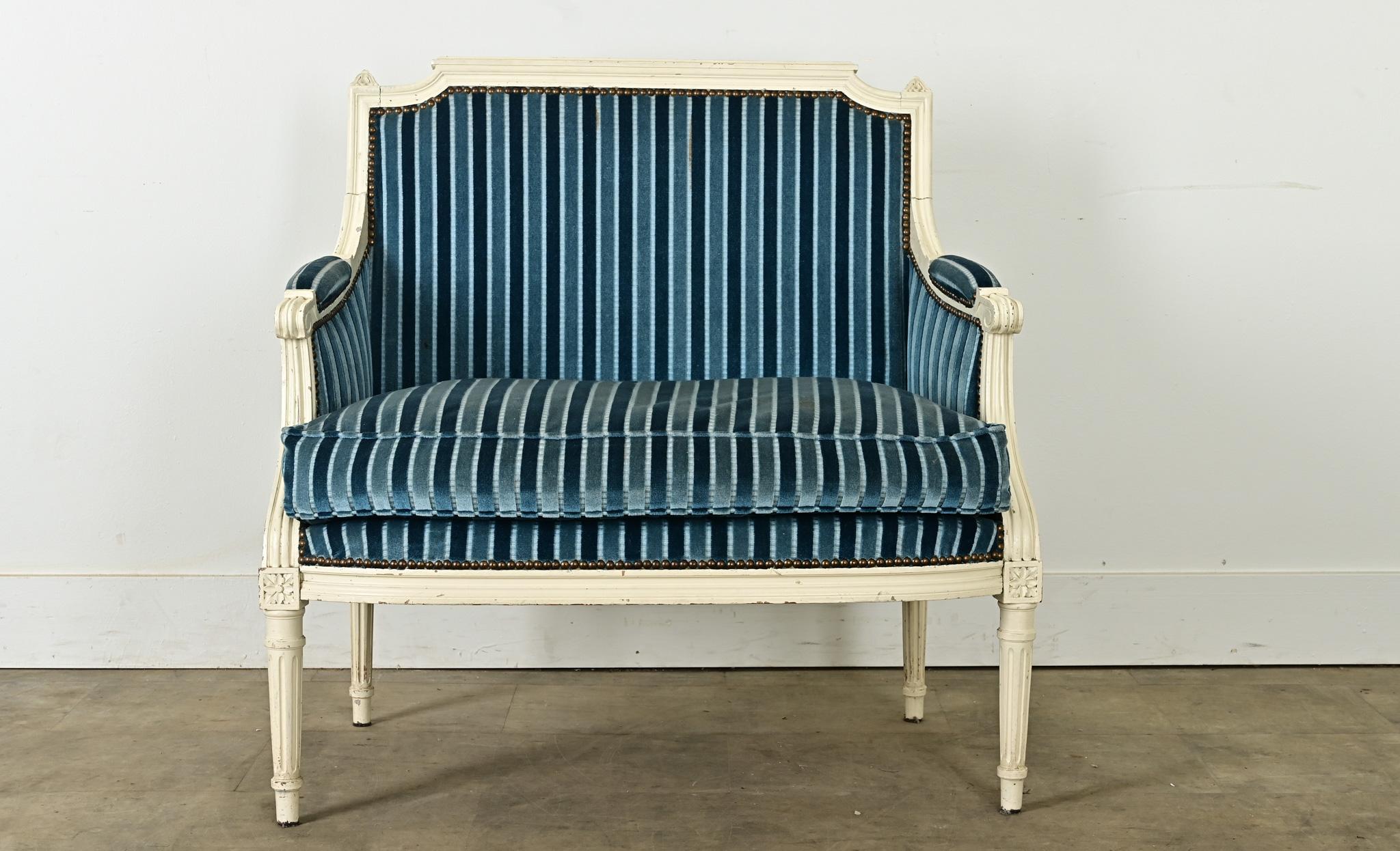 A French Louis XVI marquise bergère, better known as a chair and a half, from the 19th century. This example offers timeless sophistication, the lines and ornamentation are spare allowing the gorgeous blue striped striped upholstery to shine. Down