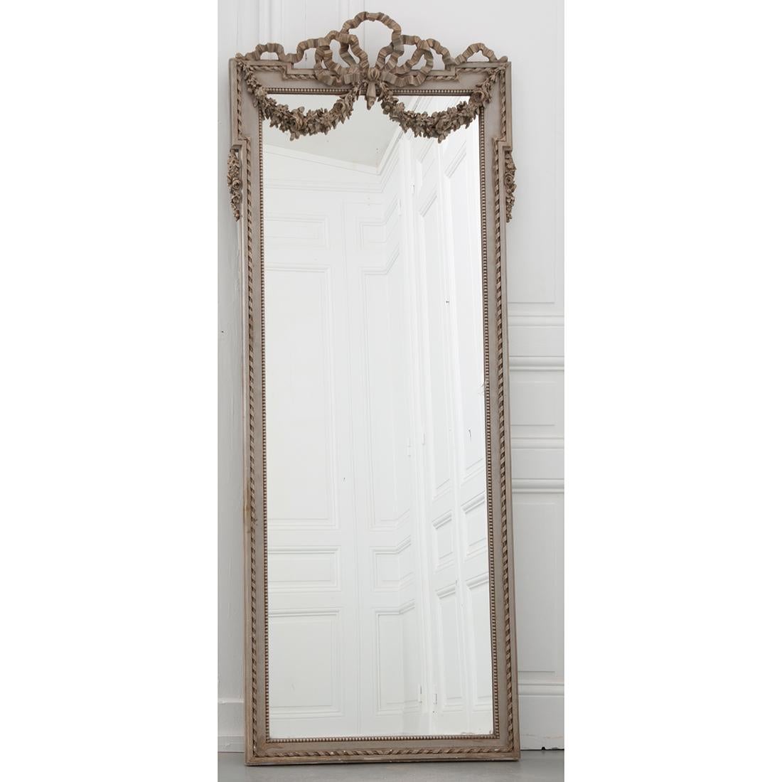 French Louis XVI style painted mirror with original mercury glass. Absolutely stunning designs on this tall, gray/green mirror. Elegant ribbons flow across the top of the mirror frame while floral swags drape over the top of the mirror. The frame is