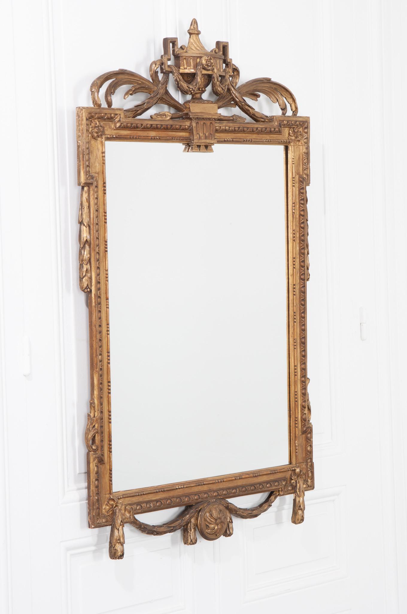 A delightful carved and painted mirror, made in Louis XVI style, 19th century, France. The mirror is crowned with a wonderfully carved crest depicting an urn, foliage and garlands. The new mirror glass is trimmed in a beautiful carved motif with