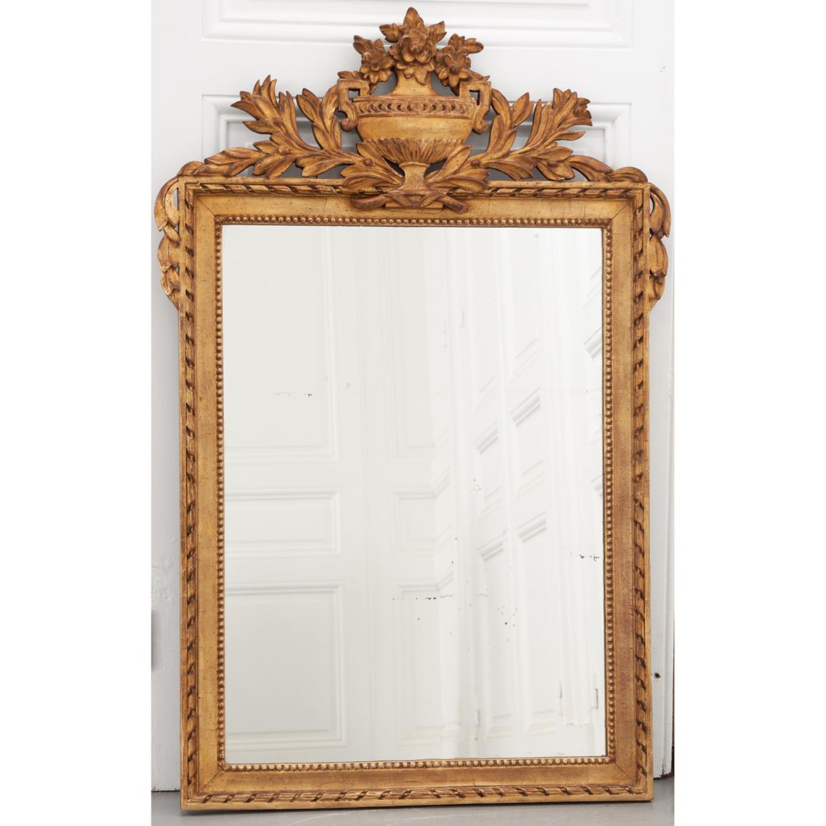 This French 19th century Louis XVI-style mirror has its original mirror plate with some aging. The crest at the top of the mirror has a floral and foliate covered urn. It is a nice petite size for a small area.