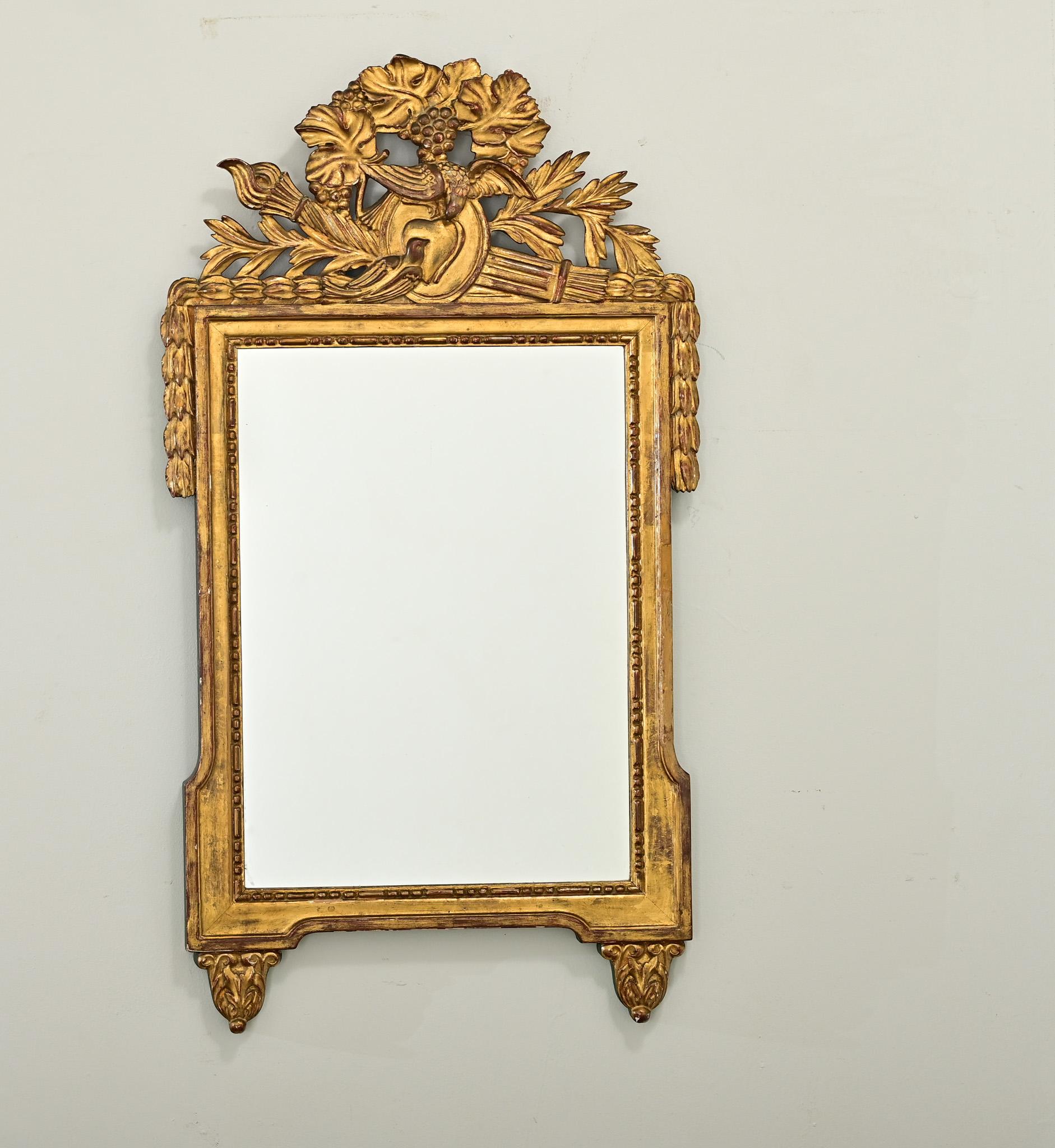 Un gran espejo francés del siglo XIX, de estilo Luis XVI, con increíbles tallas de madera dorada sobre el panel trasero pintado de verde. En la parte superior de la pieza, unas tallas foliadas de laurel y roble rodean a una pareja de tortolitos y