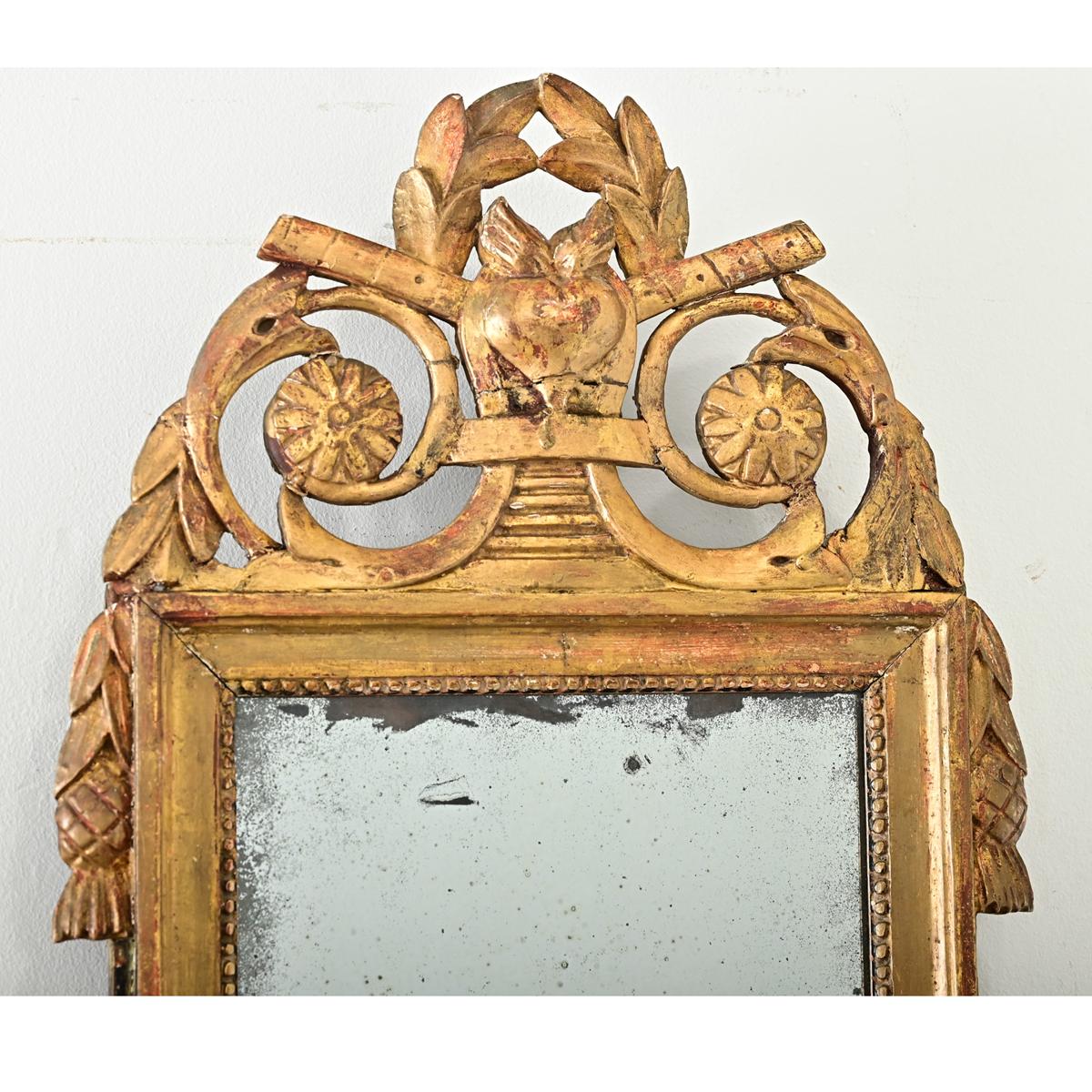 Pequeño trumeau francés dorado de estilo Luis XVI. El marco del espejo dorado y pintado tiene una cresta tallada con un corazón llameante y hojas de laurel. La placa original del espejo está descolorida, brilla y está rodeada por el ribete de
