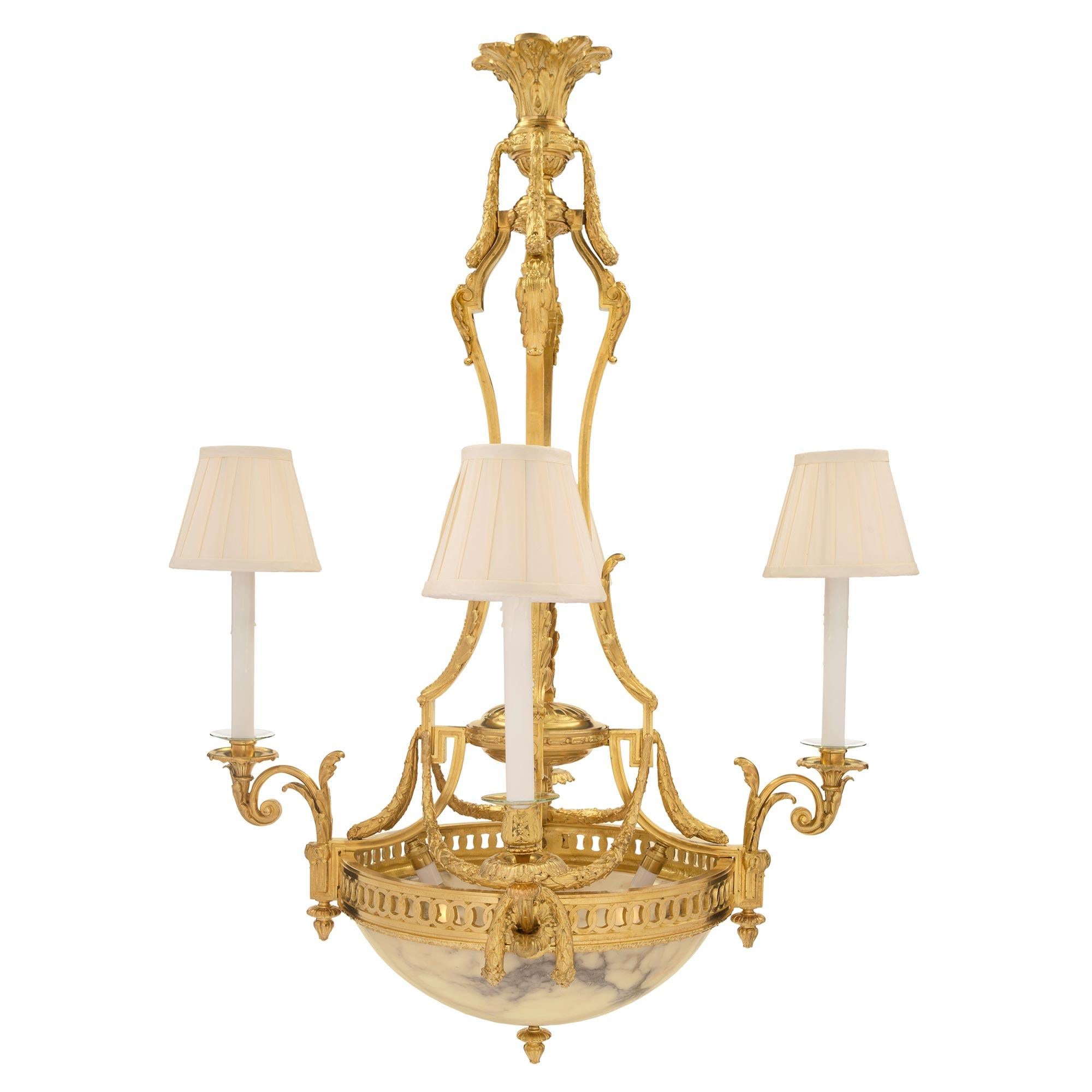 An exquisite French 19th century Louis XVI st. ormolu and alabaster four arm, six light chandelier. The chandelier is centered by a charming bottom ormolu acorn finial below the striking alabaster bowl which houses two interior light bulbs offering