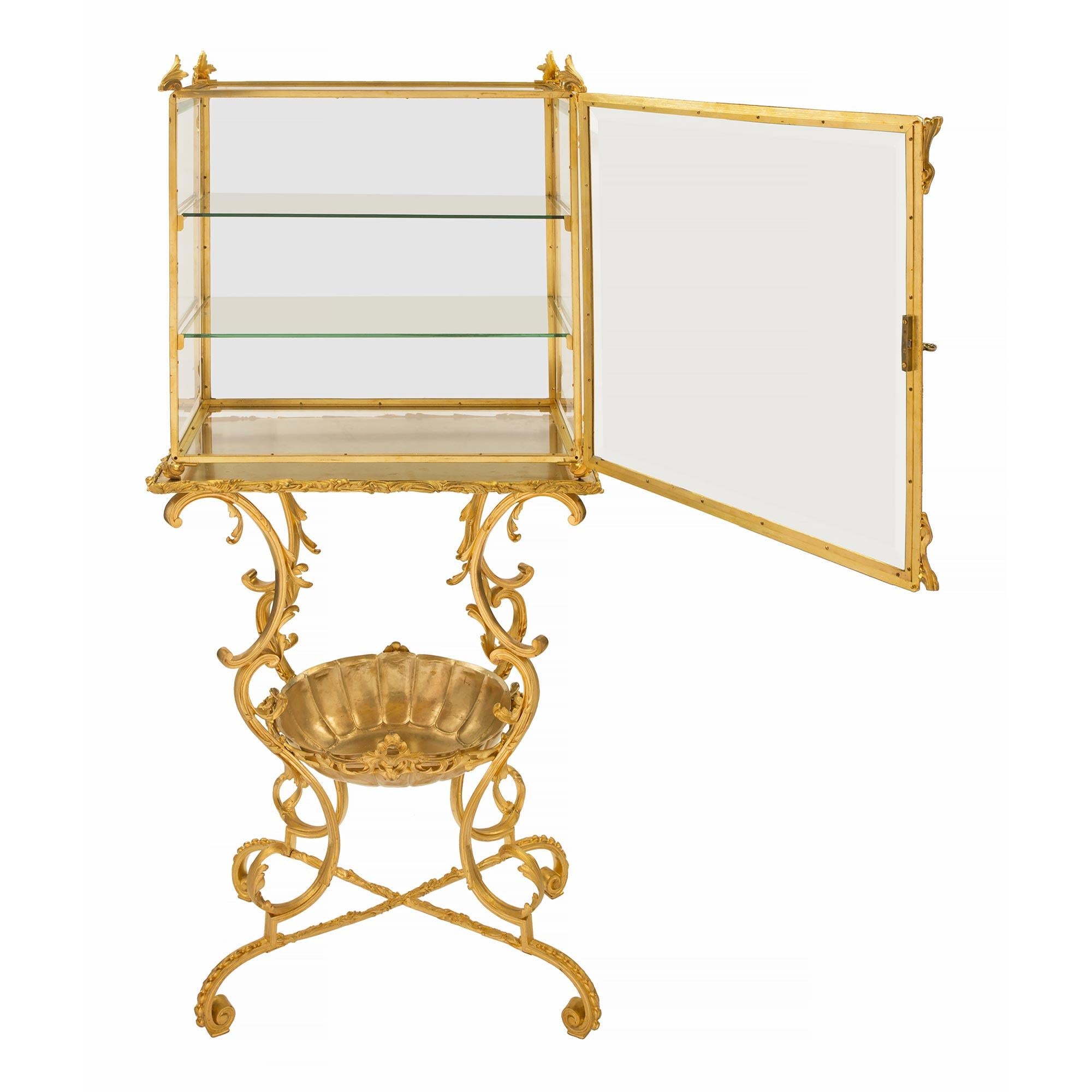 A striking and most unique French 19th century Louis XIV st. ormolu and glass display vitrine. The vitrine is raised by fine scrolled beaded feet joined by an X stretcher. The base displays a most decorative and superbly curved design with scrolled