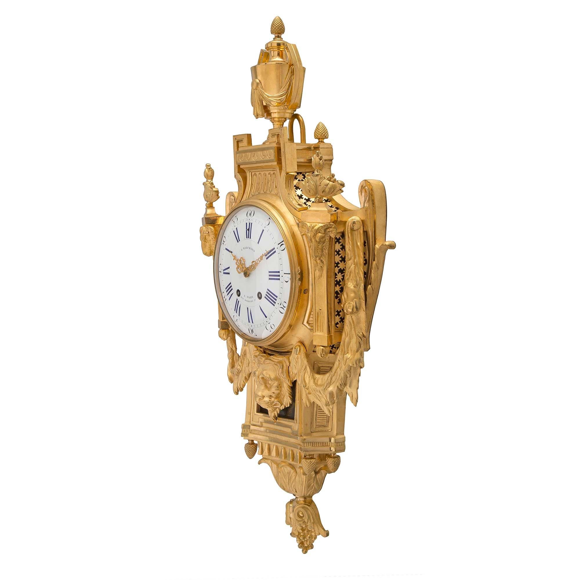 Superbe horloge cartel en bronze doré de style Louis XVI du 19ème siècle, par L. Marchand. L'horloge présente un fin fleuron inversé à base de baies et de feuillages finement gravés, sous quatre fleurons à gland. Au-dessus, une belle et