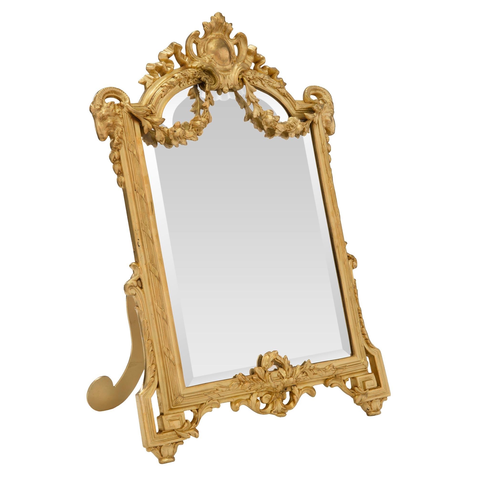 A charming and most elegant French 19th century Louis XVI st. ormolu freestanding vanity mirror. The original beveled mirror plate is set within a fine mottled frame with a lovely tied fluted border. At the base are Greek key shaped supports with