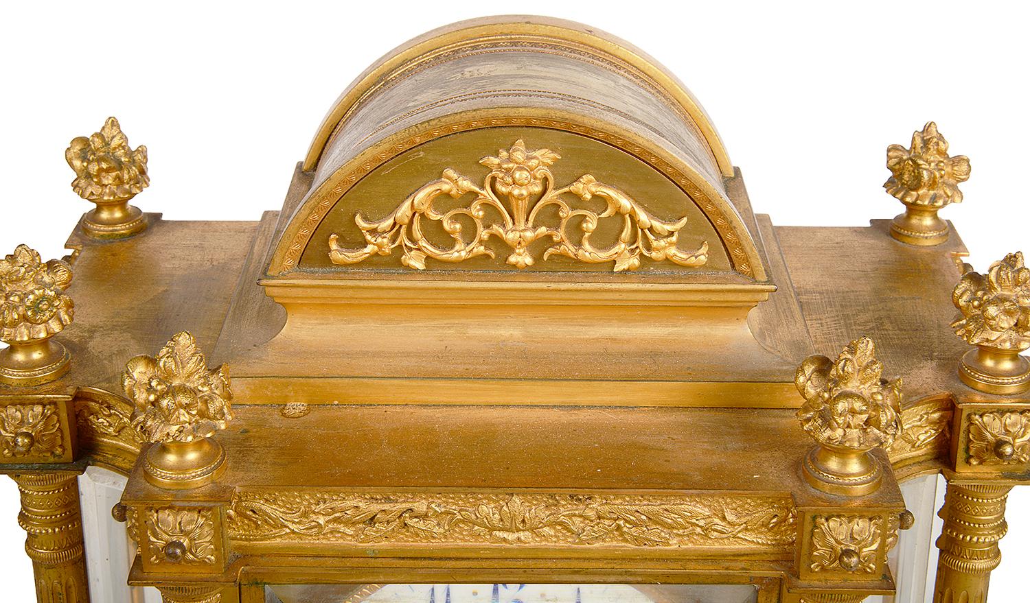 A good quality 19th century French gilded ormolu mantel clock, having an arched pediment with scrolling detail, six floral finials above column supports, beveled glass panels, a white enamel clock face with an eight day duration movement that chimes