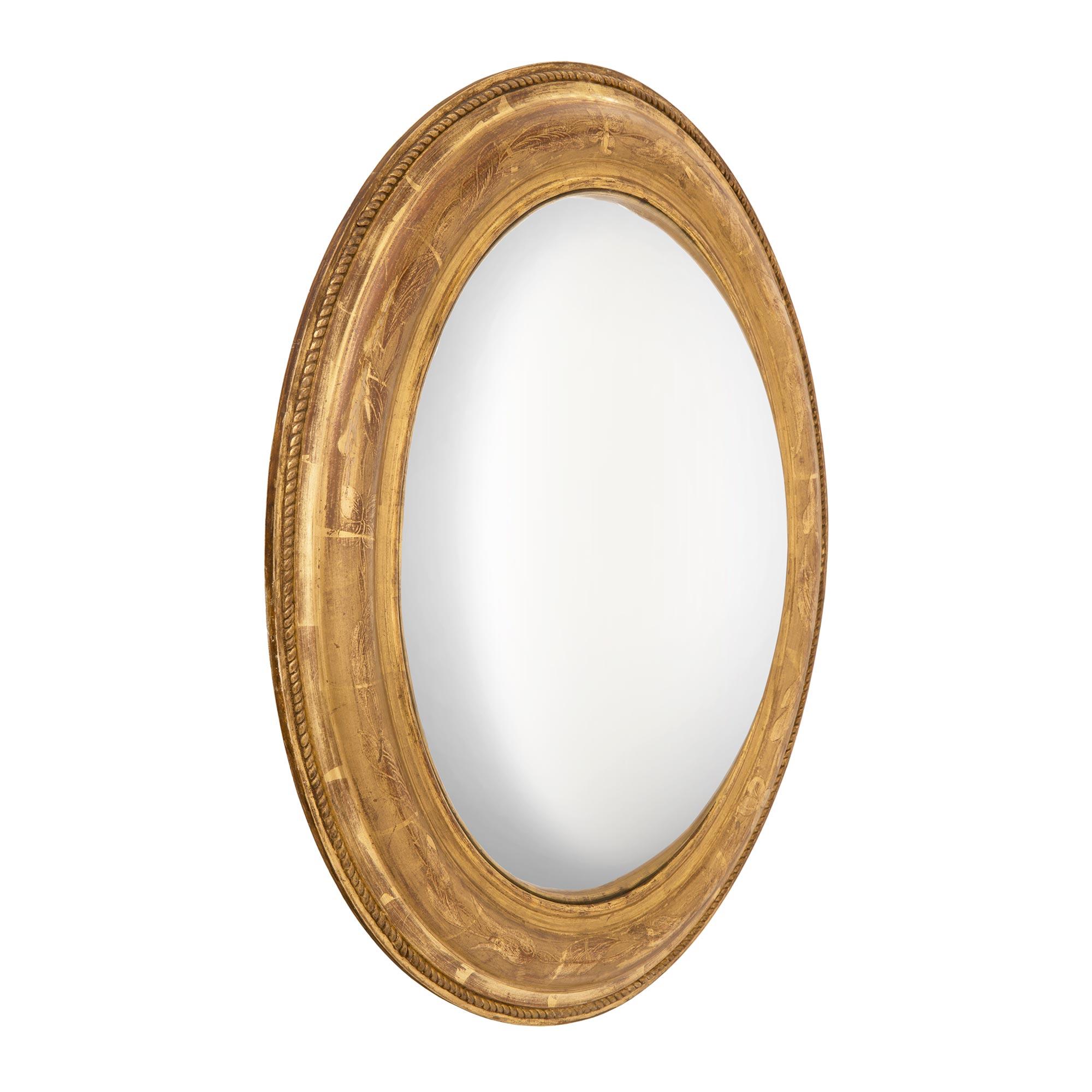A lovely French 19th century Louis XVI st. oval giltwood mirror. The convex, or fisheye, original mirror plate is fitted within a most decorative mottled frame. The frame displays richly detailed carved foliate designs throughout and fine carved