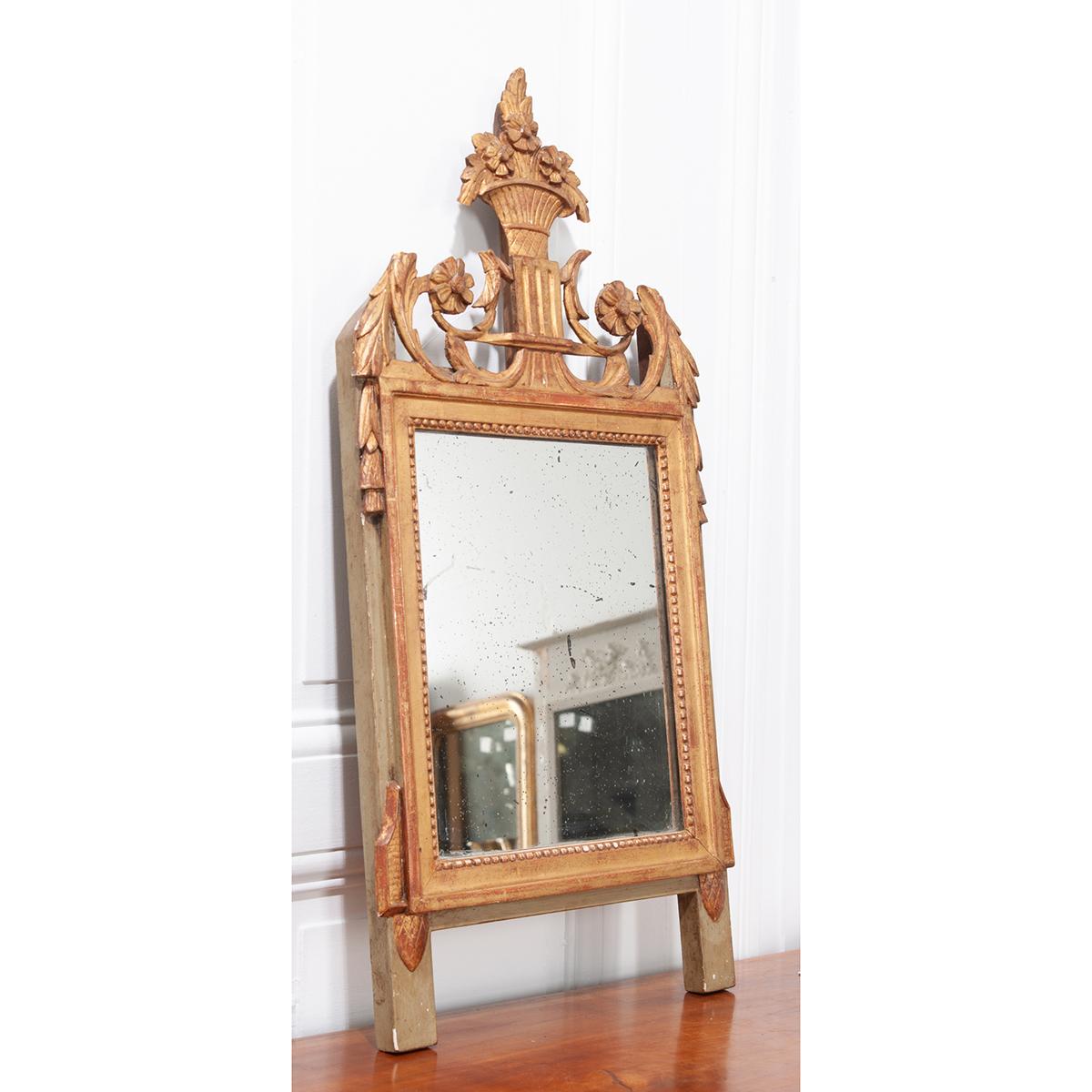 A darling, carved giltwood mirror. This petite mirror has a wonderful crest that features floral and foliate carvings, scrolled filigree and acanthus leaves. The original glass remains intact and adds great character with tons of foxing. The glass