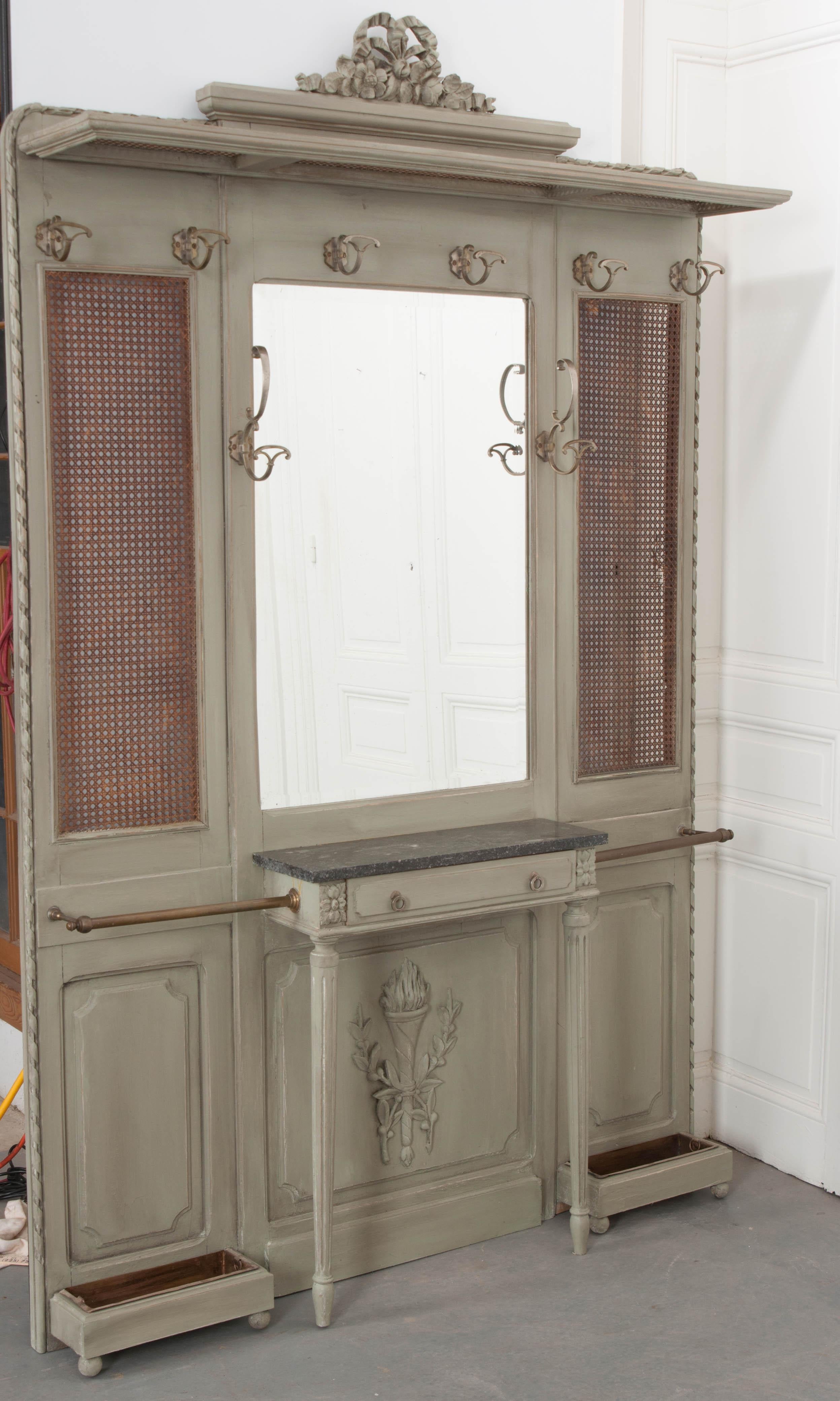 An impressive Louis XVI style hall tree from 19th century France. The antique has a centrally located mirror with an panel on each side. Each panel is backed in woven cane and has a brass rail and drip pan for storing umbrellas. The mirror has its