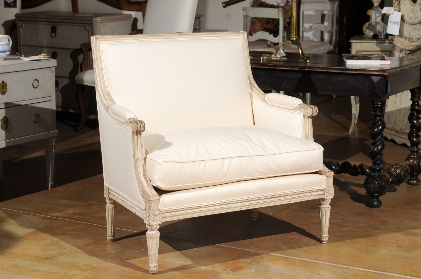 A French Louis XVI style painted wood Marquise chair from the 19th century, with carved rosettes, fluted legs and newer upholstery. Created in France during the 19th century, this Louis XVI style Marquise (meaning wider than a typical bergère)