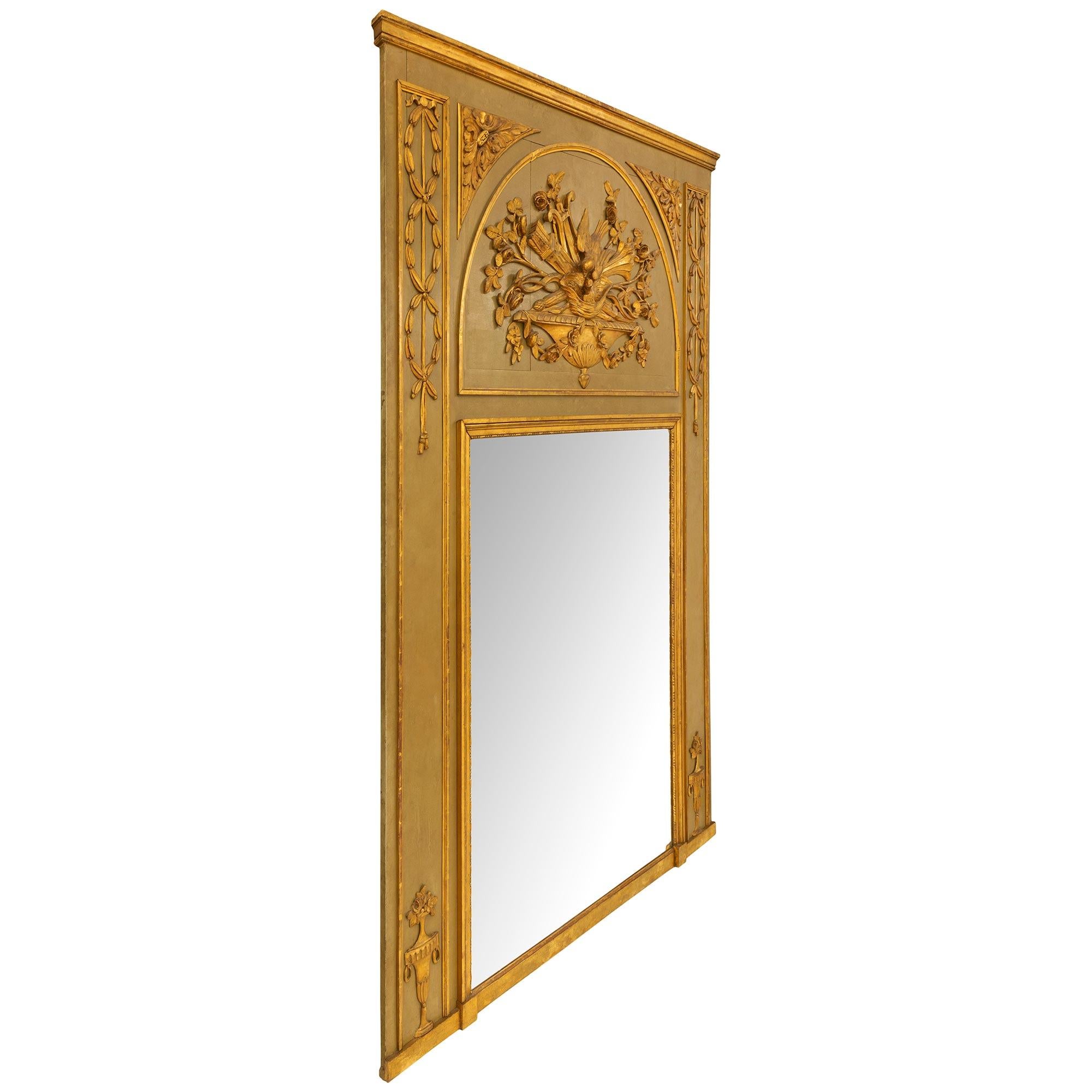 An extremely elegant French 19th century Louis XVI st. patinated and giltwood Trumeau. The olive green patinated frame has two finely carved giltwood urns with flowers at each bottom corner. Above are interlocking laurel bands with a ruban noué