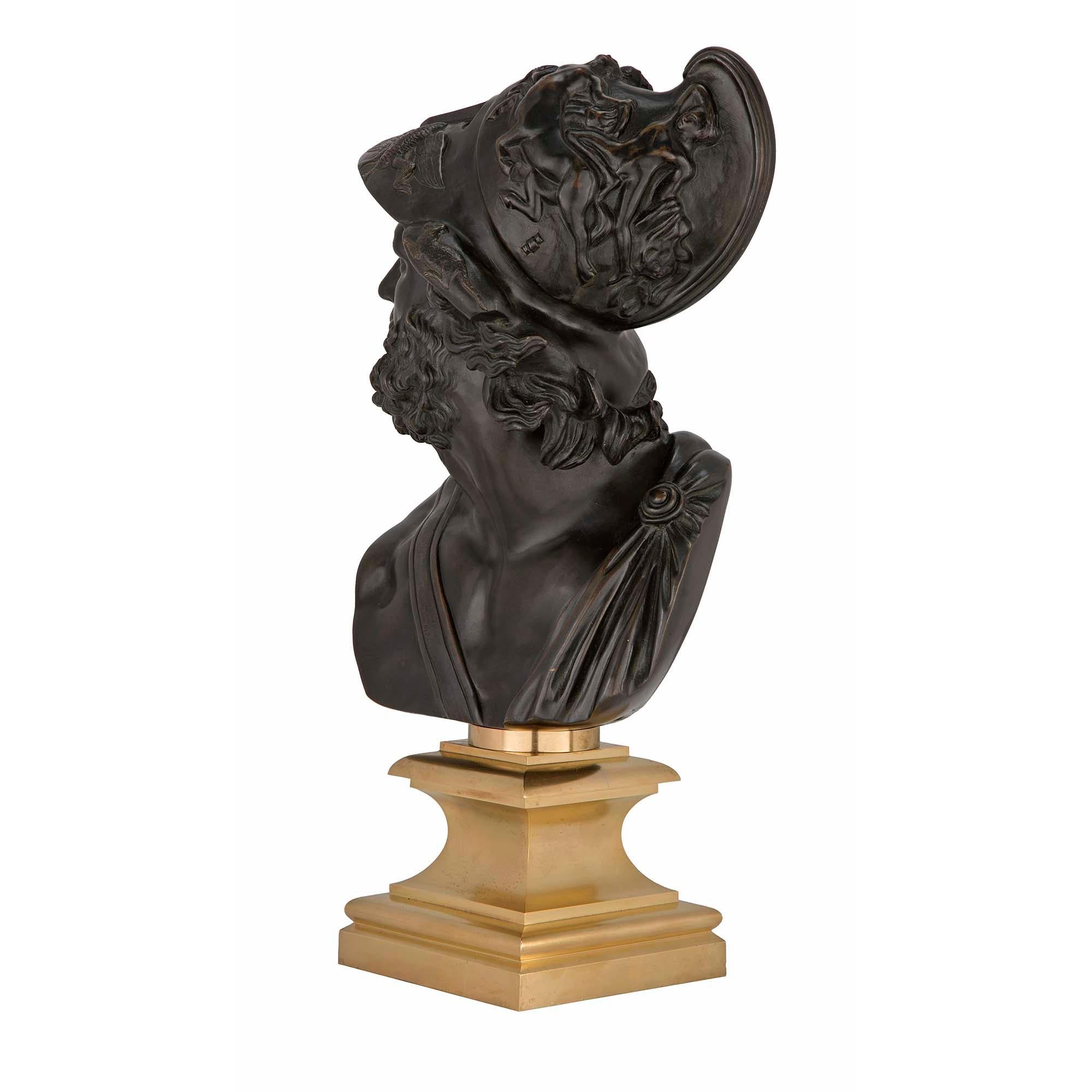 A striking French 19th century Louis XVI style patinated bronze and ormolu bust of Menelaus. The bust is raised by a square ormolu base below a fine mottled socle pedestal. The richly chased patinated bronze soldier is draped in period attire tied