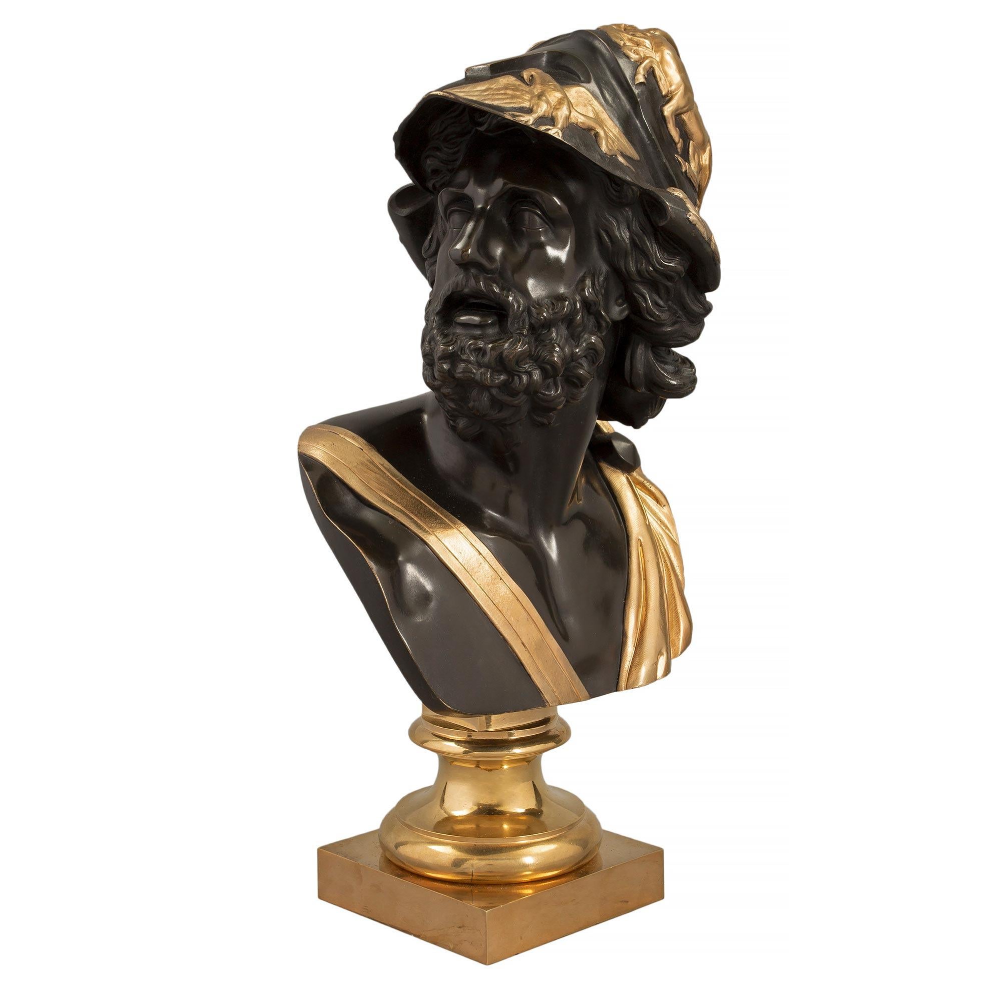 A striking French 19th century Louis XVI st. patinated bronze and ormolu bust of Menelaus. The bust is raised by a square ormolu base below a fine mottled socle pedestal. The richly chased patinated bronze soldier is draped in period attire tied at