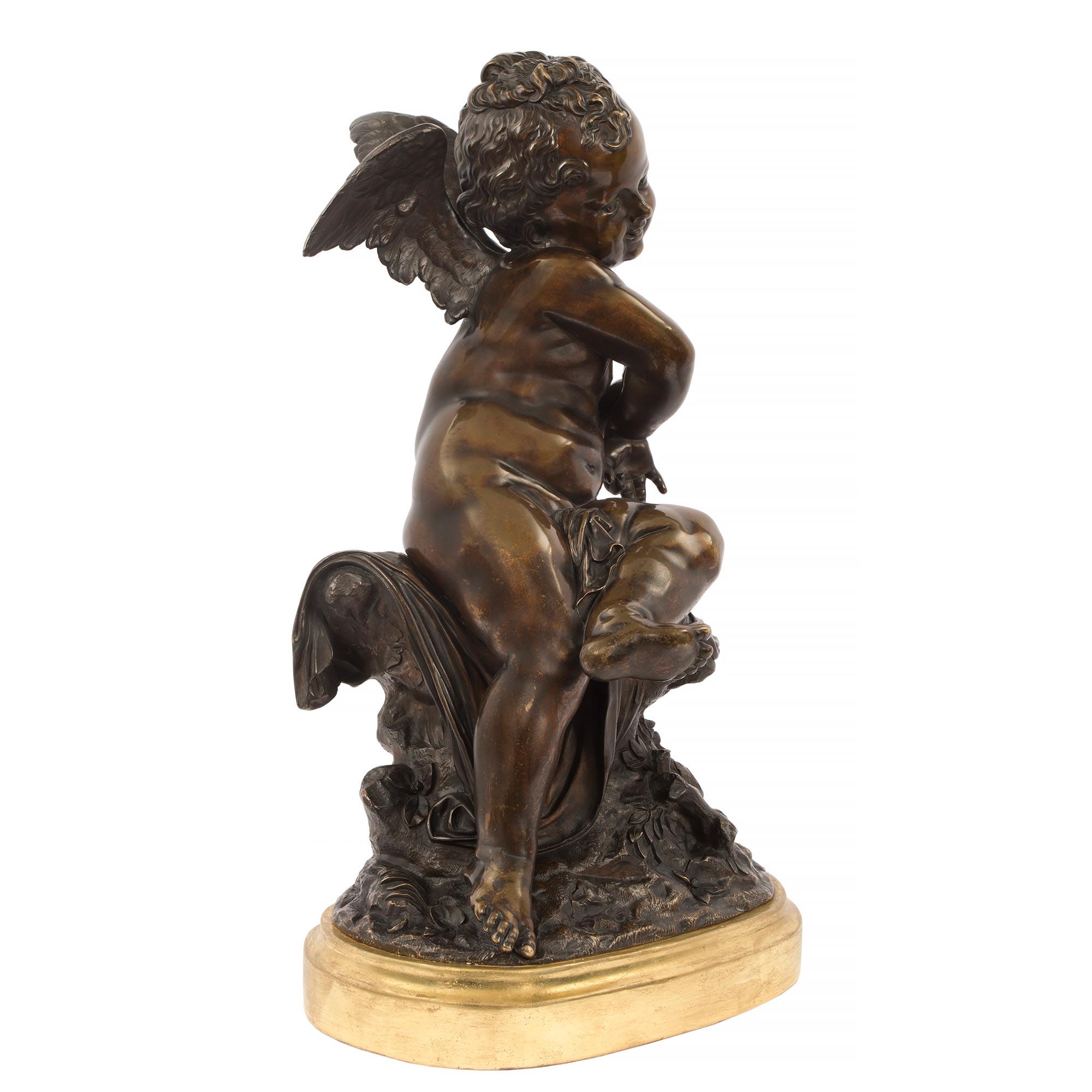 Magnifique statue en bronze patiné de style Louis XVI, signée Lemire. La statue est surmontée d'une base ovale en bois doré avec une fine bordure tachetée. Au-dessus, l'angelot ailé en bronze patiné richement ciselé est assis sur une souche d'arbre