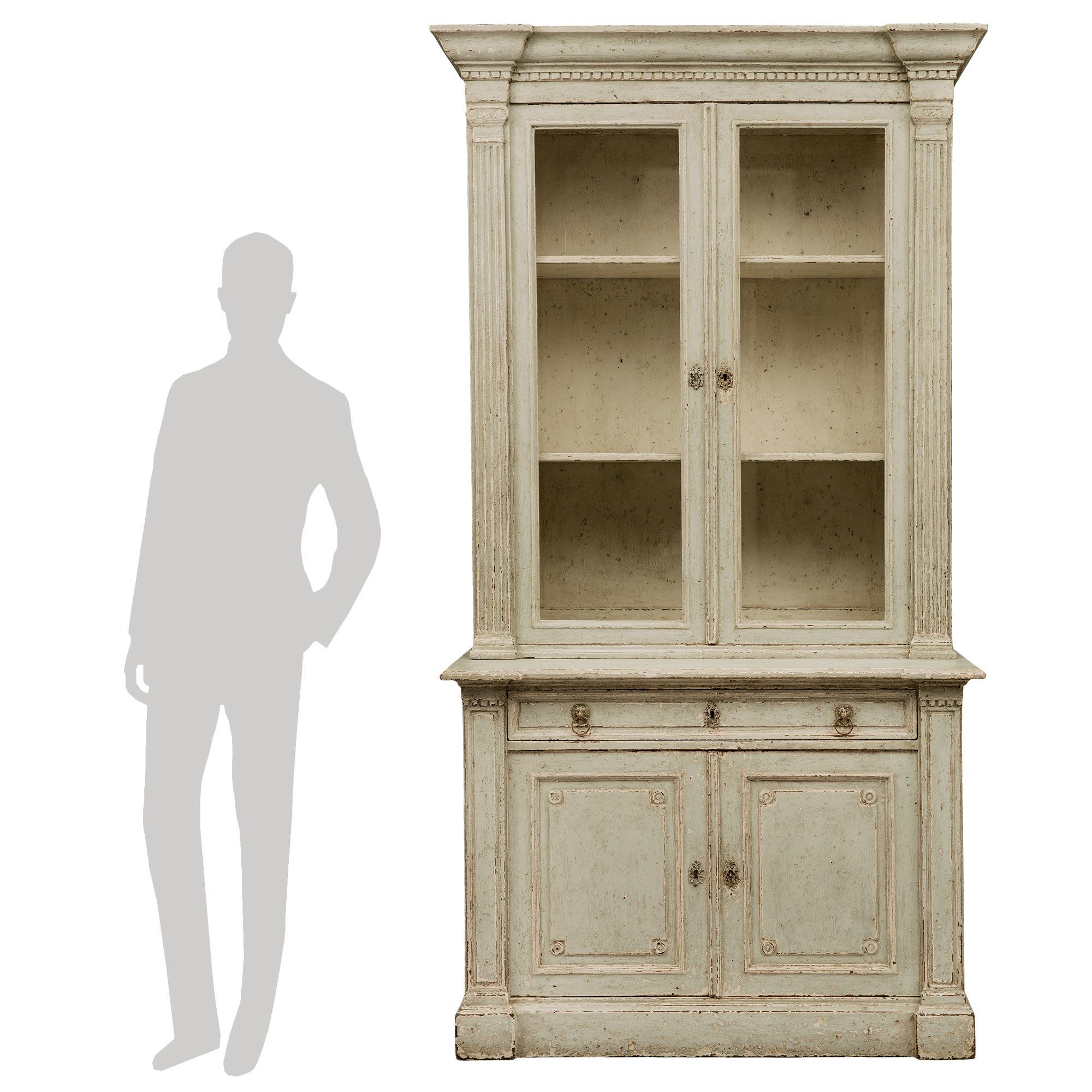 A most elegant French 19th century Louis XVI st. patinated deux corps cabinet vitrine. The vitrine is raised by a straight base with a mottled design and elegant side vertical columns with dentil molding at the top. Above is a single drawer