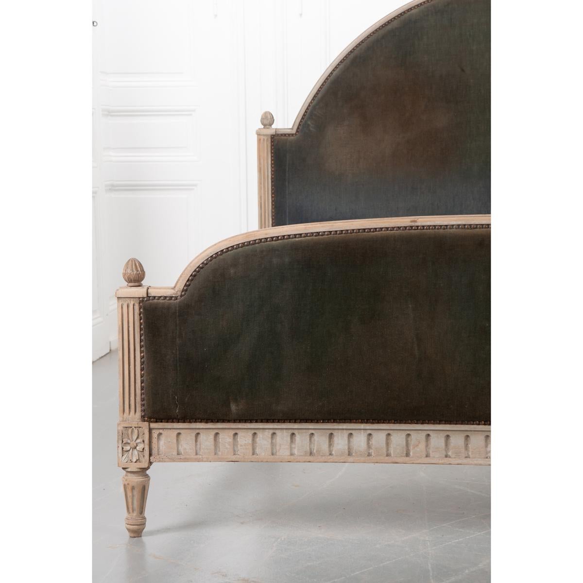 This elegant, 19th century bed is painted and upholstered. It has an off white, greenish paint highlighting the details and a very worn soft blue velvet for the upholstery accented by brass nailhead trim. The headboard has a nice big arch framed by