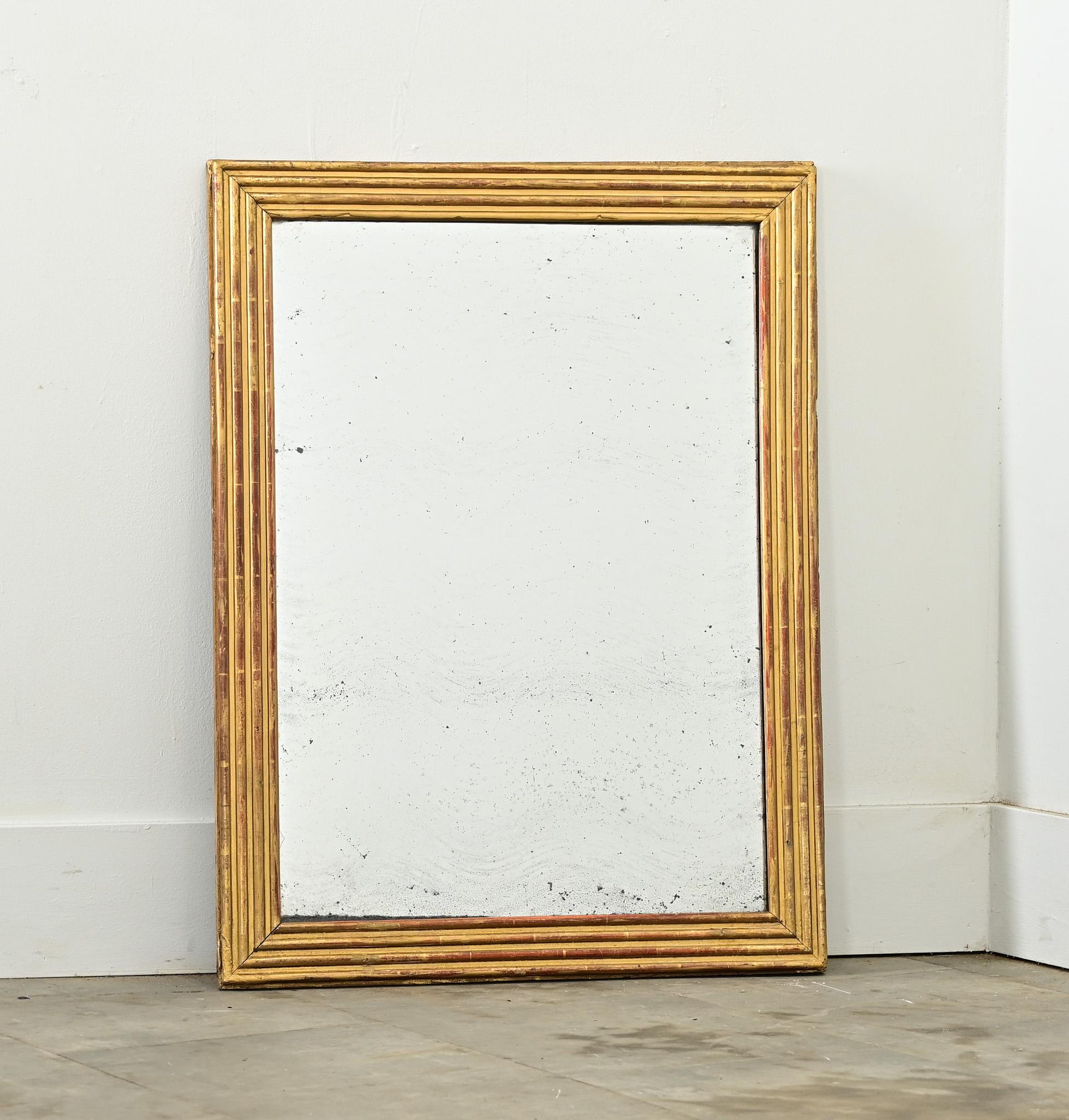 Les larges moulures à cannelures qui entourent ce miroir mural doré français du XIXe siècle constituent une surface idéale pour refléter l'éclat de la feuille d'or, aujourd'hui patinée avec une fine texture de craquelure. Symétrique pour un montage