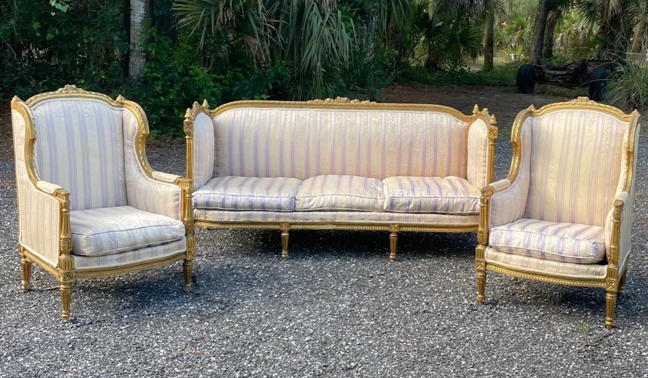 French 19th Century Louis XVI Style Settee and Bergeres A Oreilles

Exquisite gilt wood carved French Louis XVI style Parlor Suite, comprised of a
Settee and two Bergers a Oreilles. They are created in France during the turn of the century. The