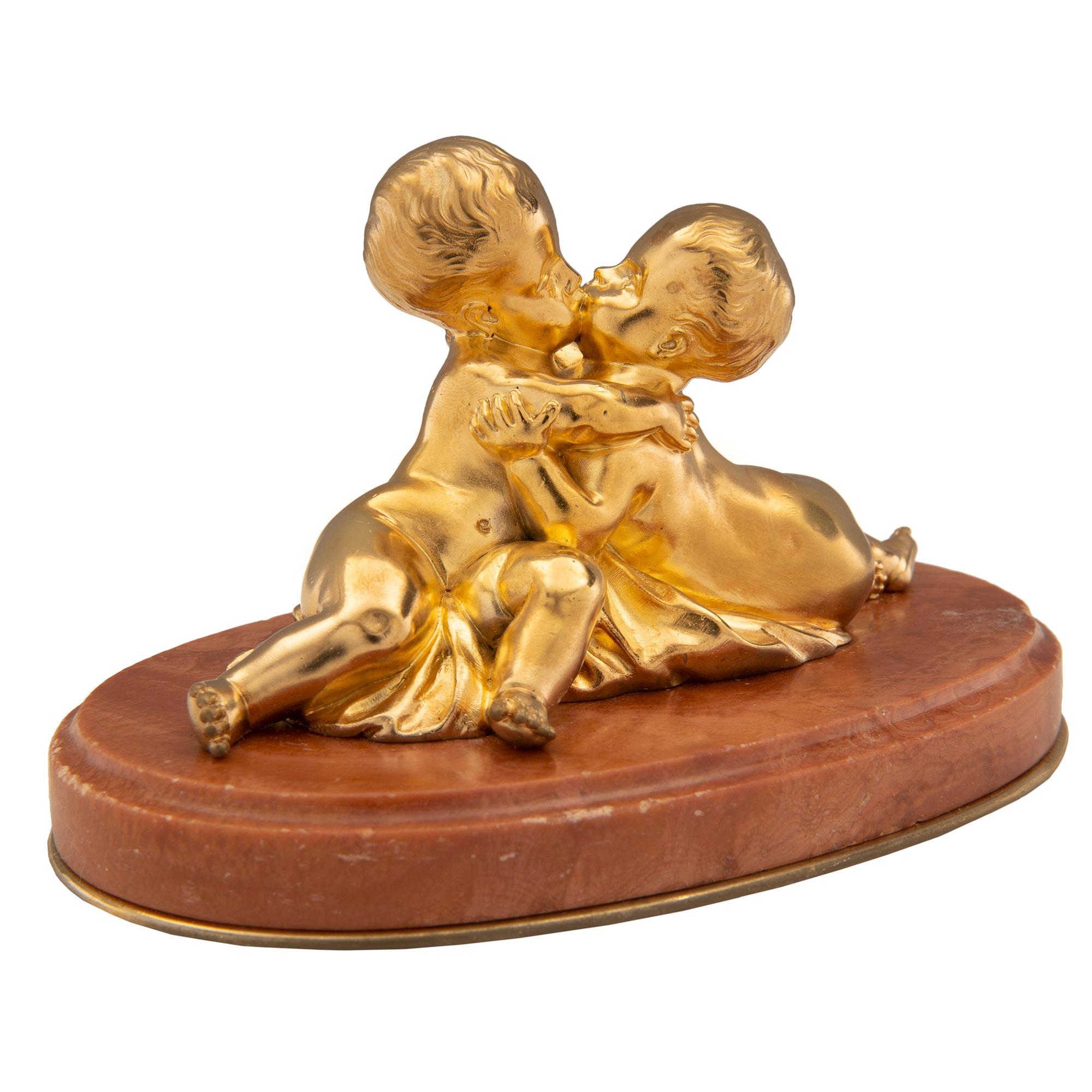 Charmante statue/ presse-papier de style Louis XVI du 19ème siècle en bronze doré et marbre Rouge Royale, signée F. Costa. La statue est surélevée par une base ovale en Rouge Royale avec une bordure mouchetée et un fin filet de fond en bronze doré.