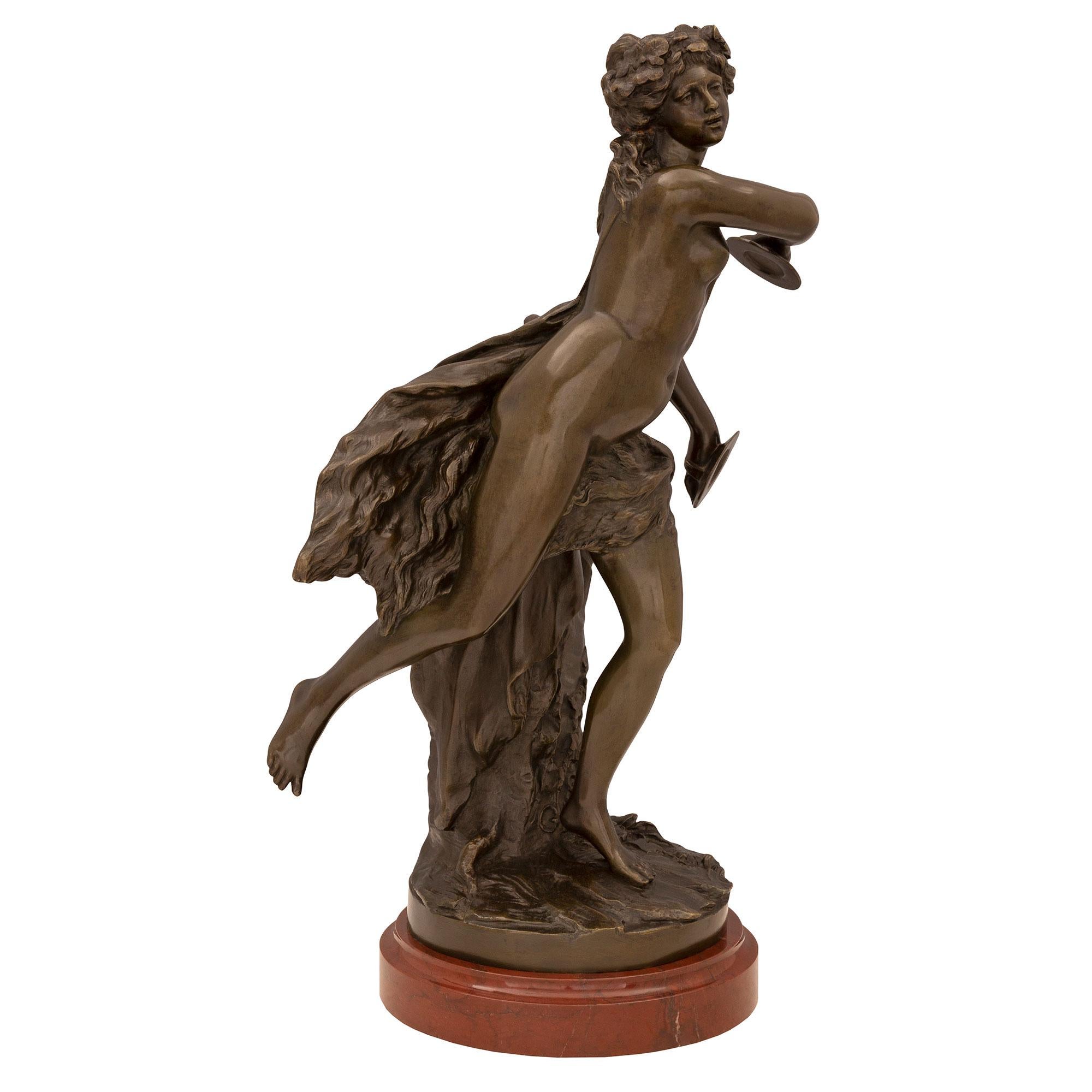 A graceful French 19th century Louis XVI st. patinated bronze and Rouge Griotte marble statue of a maiden dancing with cymbals, signed Clodion. The statue is raised by a circular Rouge Griotte marble base with a fine mottled border. The wonderfully