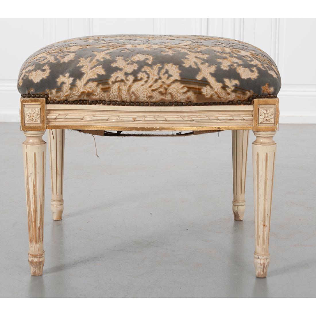 A charming, antique European stool. The cut velvet upholstery cushion has nailhead trim and sits atop a carved apron with floret dies at the four corners. The whole is raised on fluted, tapering legs. The stool has a soft, quatrefoil shape and is