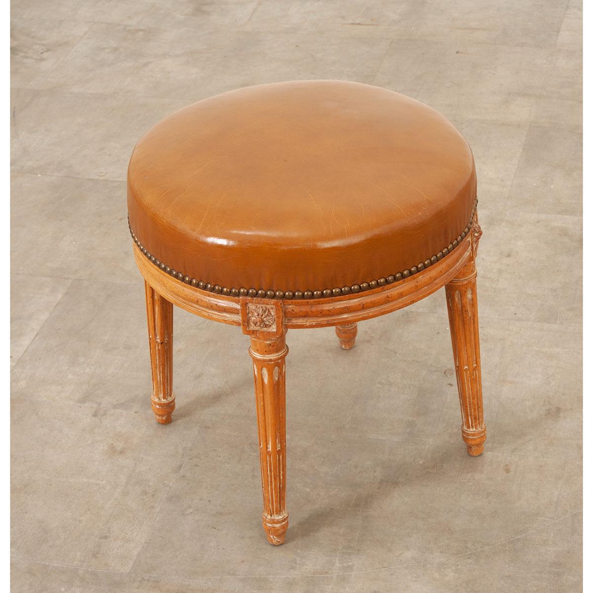 A beautiful vintage stool perfect for any space. Made in France, this 19th century stool has a brightly colored leather upholstered seat, atop four elegantly fluted and tapered legs with brass nailheads. There is a floral design carved into each