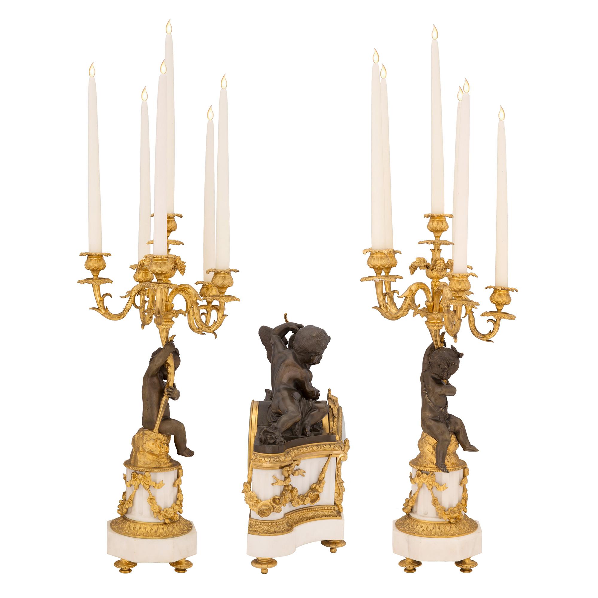 An exquisite French 19th century Louis XVI st. white Carrara marble, patinated bronze and ormolu, three-piece garniture set, signed ‘Raingo Freres’. Each piece is raised by elegant topie shaped ormolu supports below Carrara marble bases. The clock