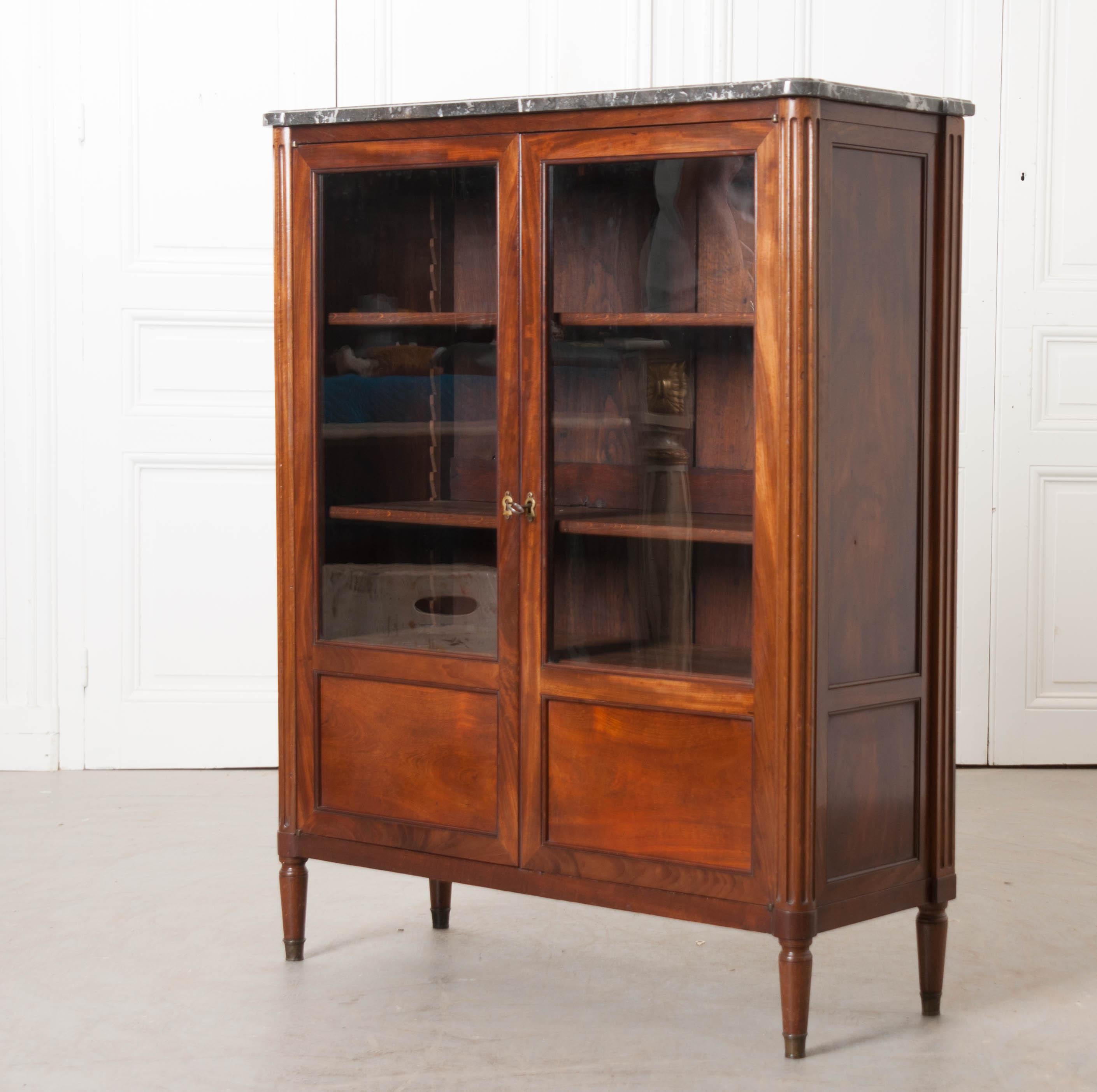 This diminutive Louis XVI-style vitrine, or bookcase, circa 1840s, was found in France and features a charcoal marble top with white veining over a pair of partially glazed and paneled doors, fluted turret corners, and raised on toupie feet. This