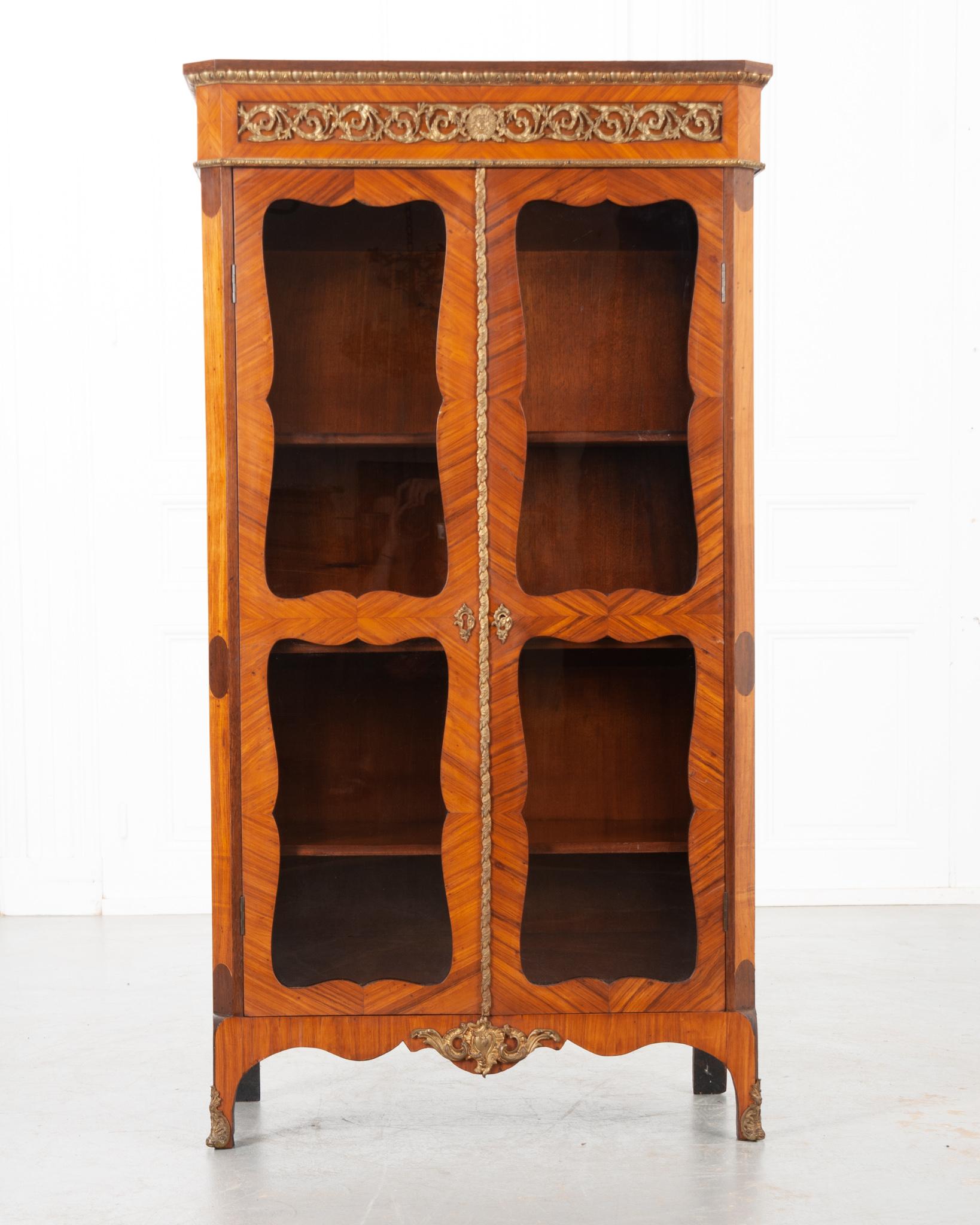 This stunning vitrine is dripping with antique elegance and character! Made in the style of Louis XVI in France circa early 1900’s. The incredible bookmatched veneer has gained a vibrant patina over the last more than a century. Although petite,
