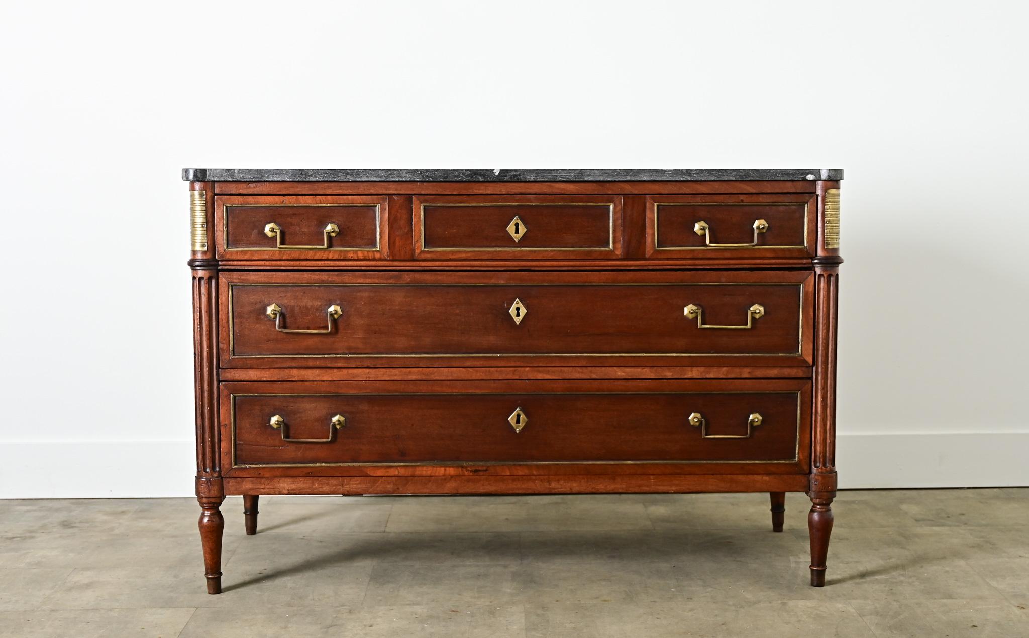 A gorgeous Louis XVI style, marble-topped walnut commode from France (late 19th century) with transitional details that could suit a wide range of decorating tastes today. The dark stone top exhibits a random sprinkling of tiny fossils among