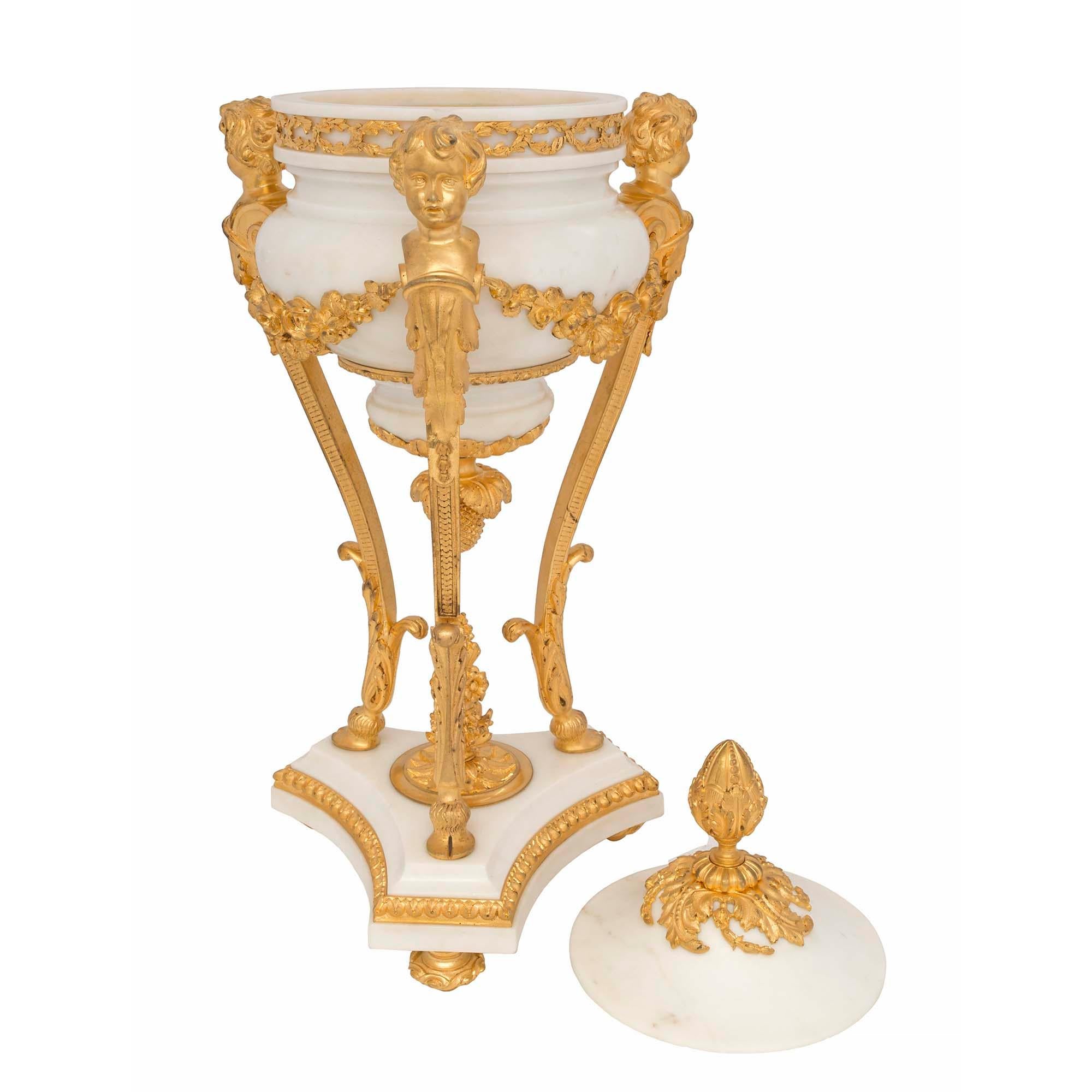 A spectacular and large scale French 19th century Louis XVI st. white carrara and ormolu lidded urn. The urn is raised by a concave triangular shaped base decorated by an ormolu trim all above ormolu topie shaped feet. The base has a central foliate