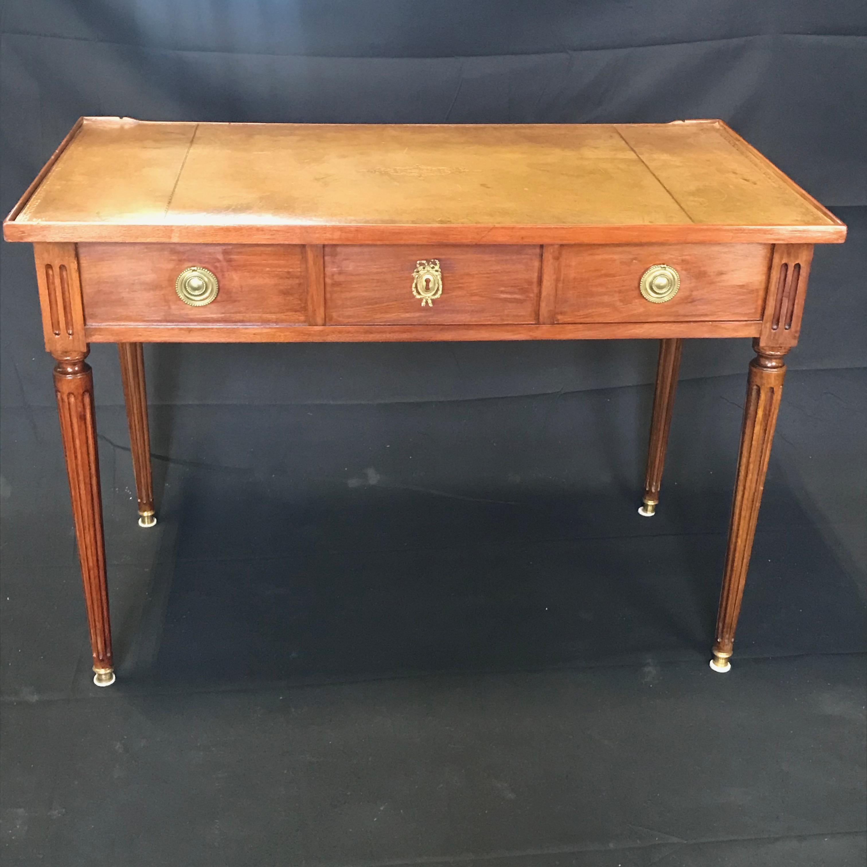 A fine French Louis XVI two sided mahogany lady's writing table or desk on reeded tapered legs with 3 drawers and pretty brass hardware. Tooled leather top is a caramel color with gold leaf. The back side looks the same as the front, but drawers are