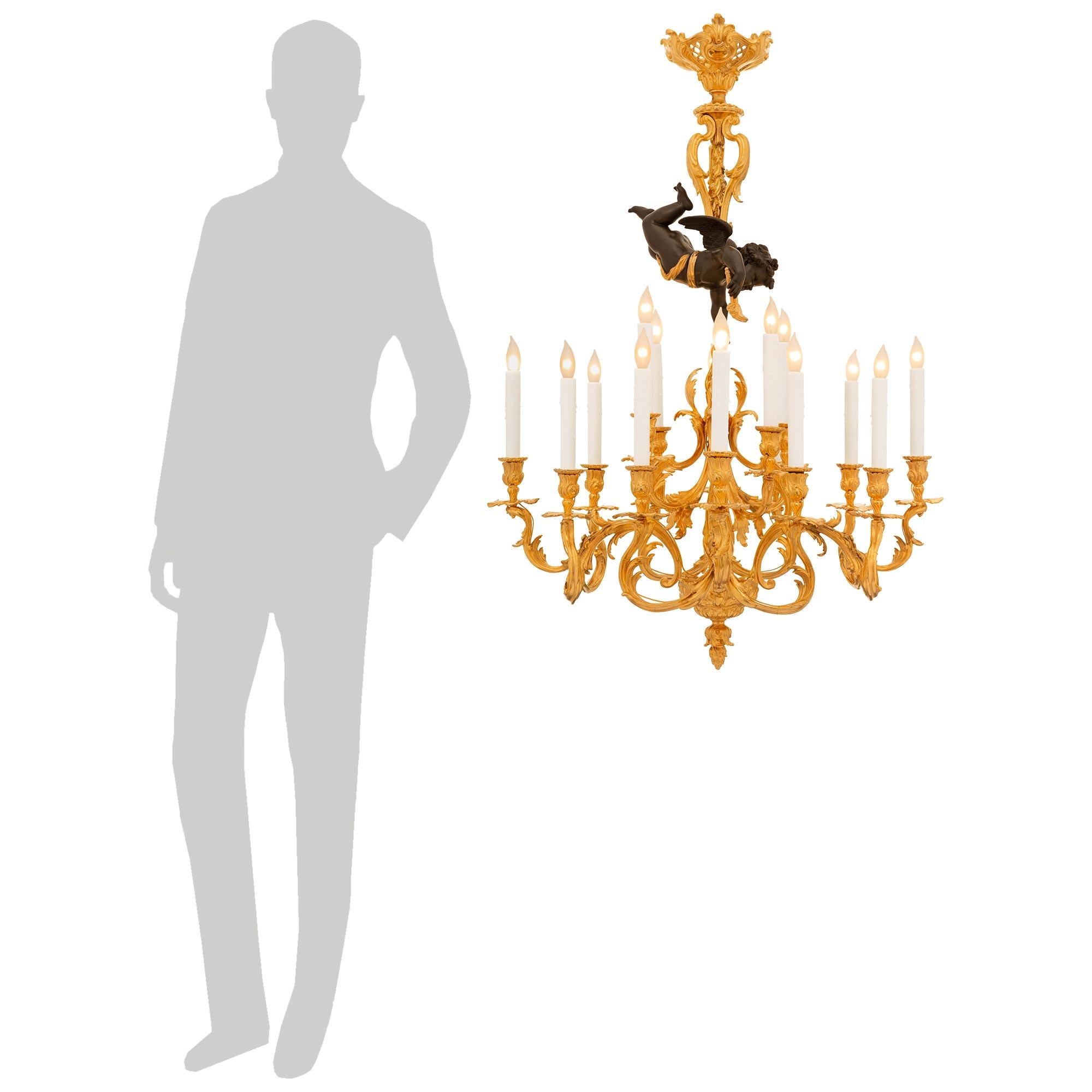 Stupendo lampadario francese del XIX secolo Luigi XVI/XV in Ormolu e bronzo patinato di alta qualità. Questo imponente lampadario a sedici luci è centrato da una ghianda situata al di sotto di una base circolare con fogliame a scorrimento. La base