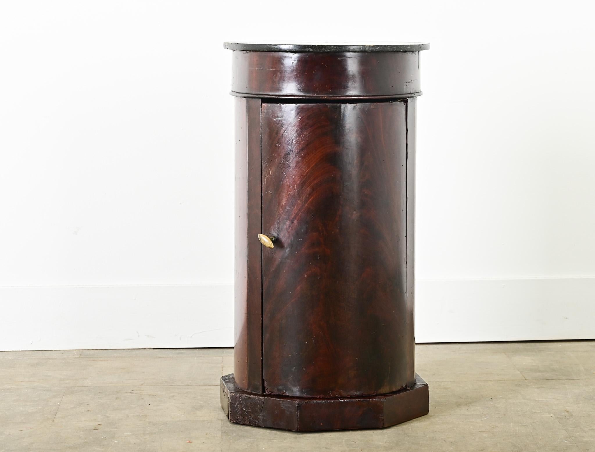 A columnar, French mahogany and marble top bedside table that offers both storage and display to fit in any room around the home. The top surface is a flat disc of black marble dusted with tiny inclusions like constellations in the night sky. Inside