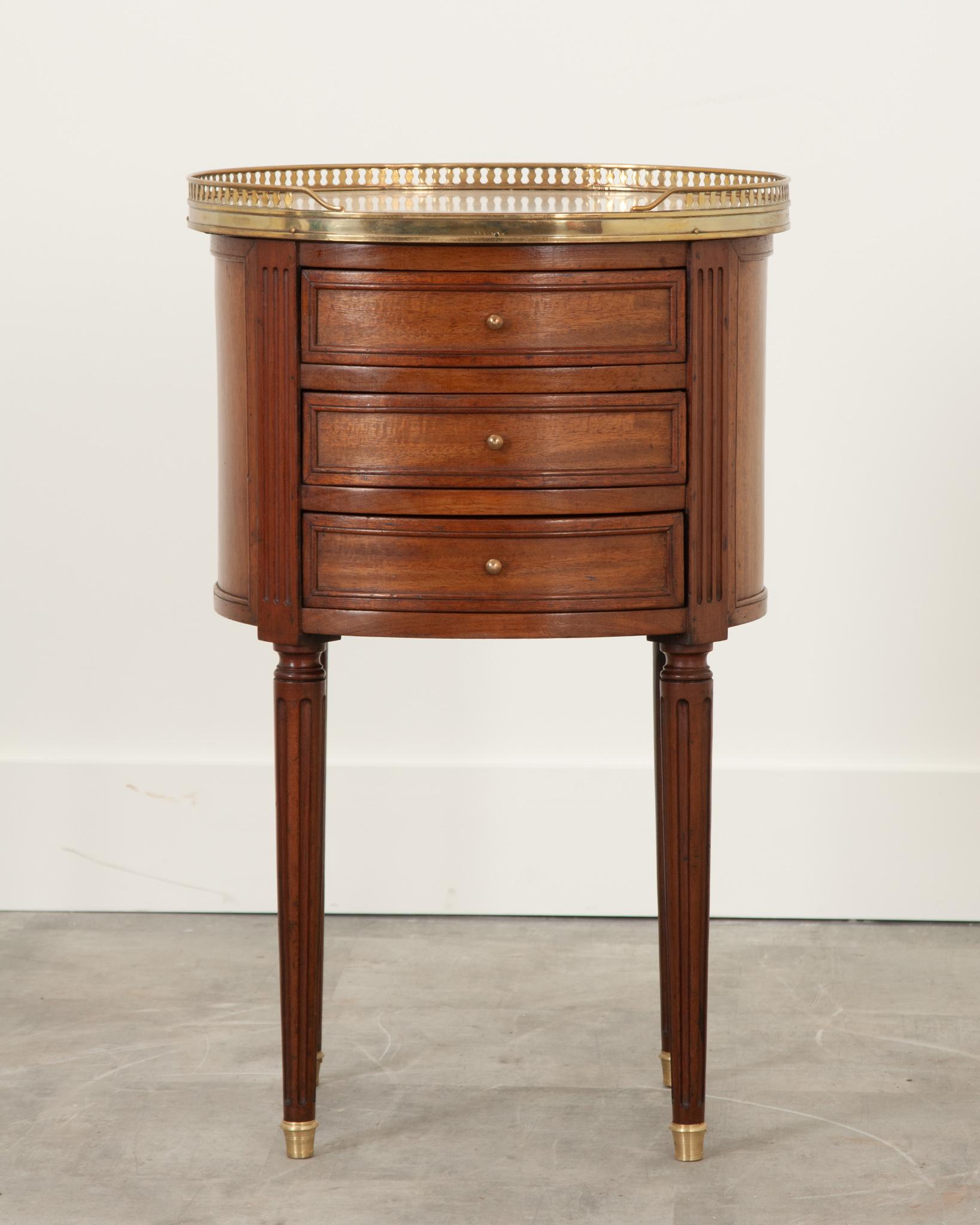 This charming mahogany bedside table was crafted in 19th century France. A breakfront pierced brass gallery surrounds the antique white marble top. Some discoloration and a hairline crack from many years of use are visible on the top. Three drawers