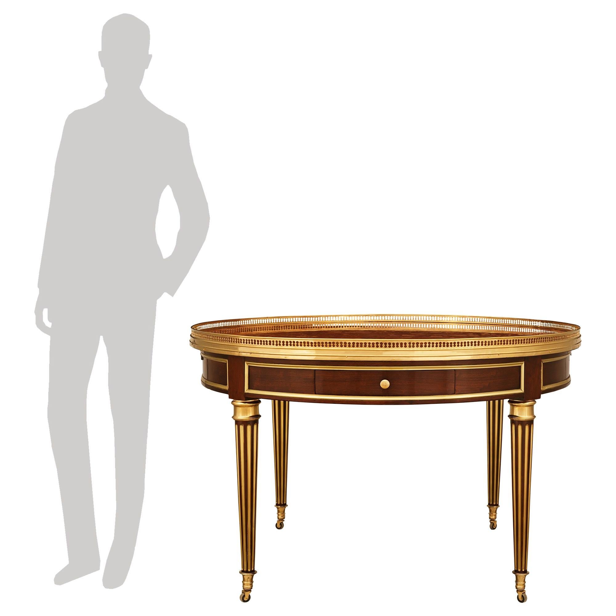 An elegant and large scale French 19th century Louis XVI st. Mahogany, Brass, Ormolu and Rosso Verona marble center table. This handsome Bouillotte table is raised on four circular Brass fluted legs with top mottled Ormolu bands, finished with