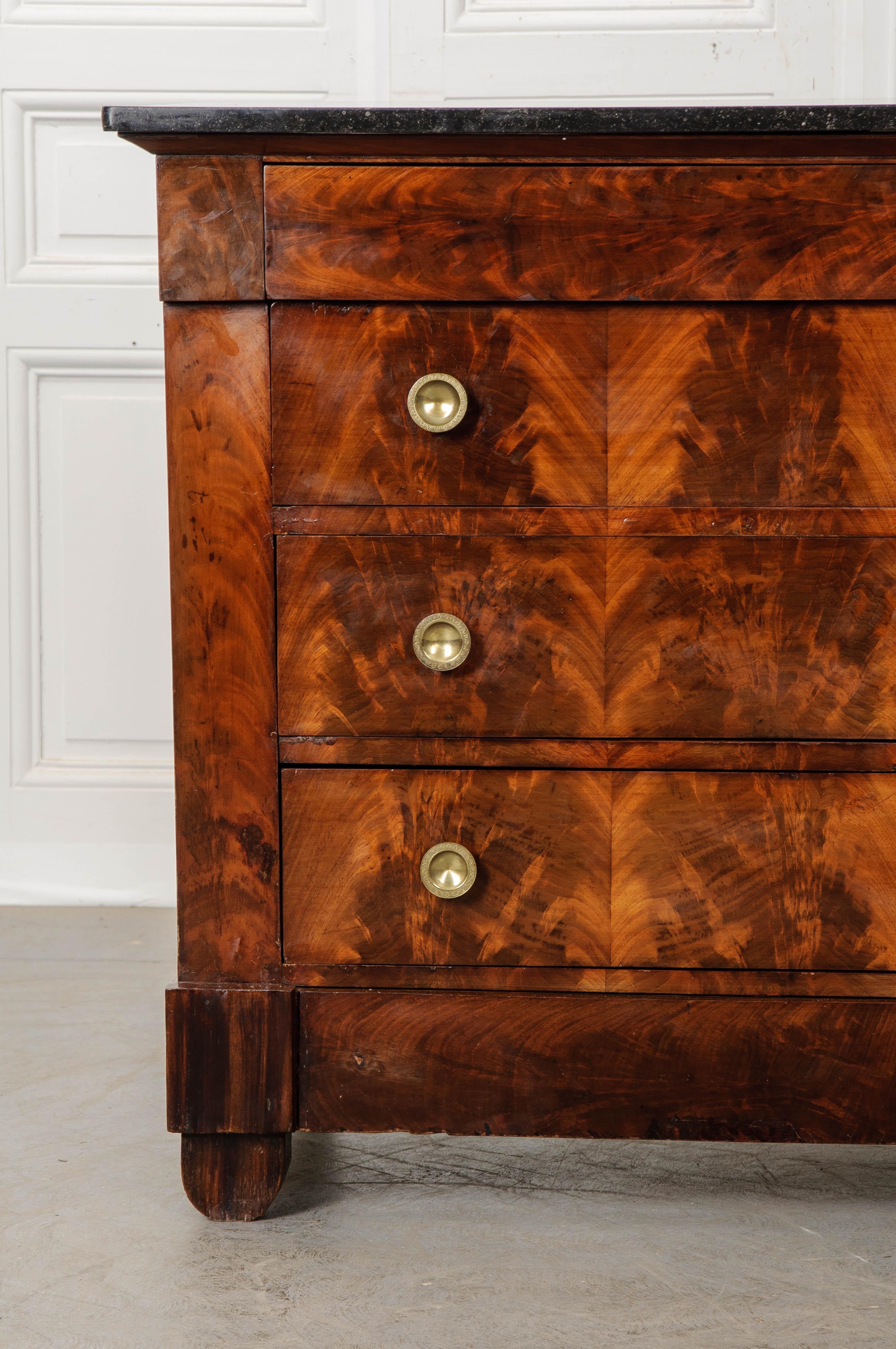 A magnificent mahogany commode, with four drawers, made in France, circa 1880. A piece of black fossil marble rests atop the case piece and is in good condition with few scratches. The commode has had its façade finished using wonderfully-marked