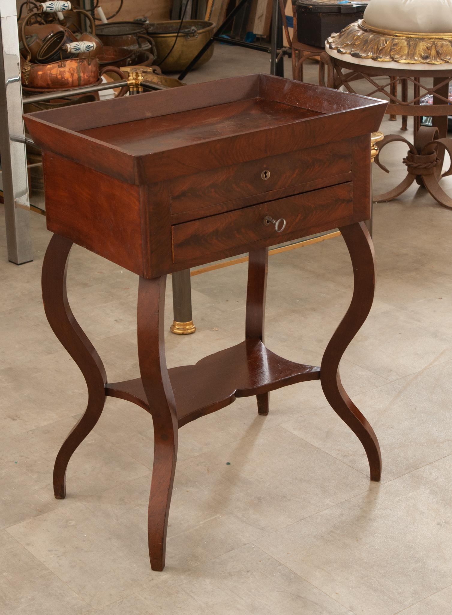 This fabulous little table was crafted in the 1850s from richly toned and bookmatched mahogany. The beveled top resembles a tray and is perfect for a small entryway or next to a sofa. Two drawers are housed within the apron; the top lock no longer