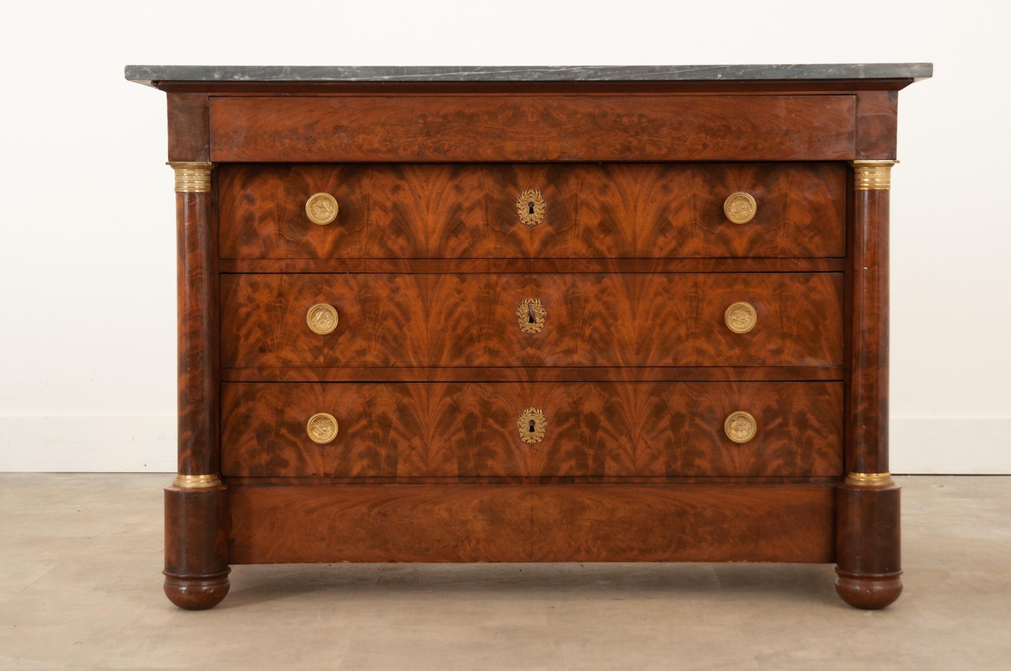 This French 19th century bookmatched mahogany commode is in wonderful antique condition. Its original charcoal and white marble top fits perfectly over the base. This commode houses four drawers for plenty of storage. The top drawer is hidden in the