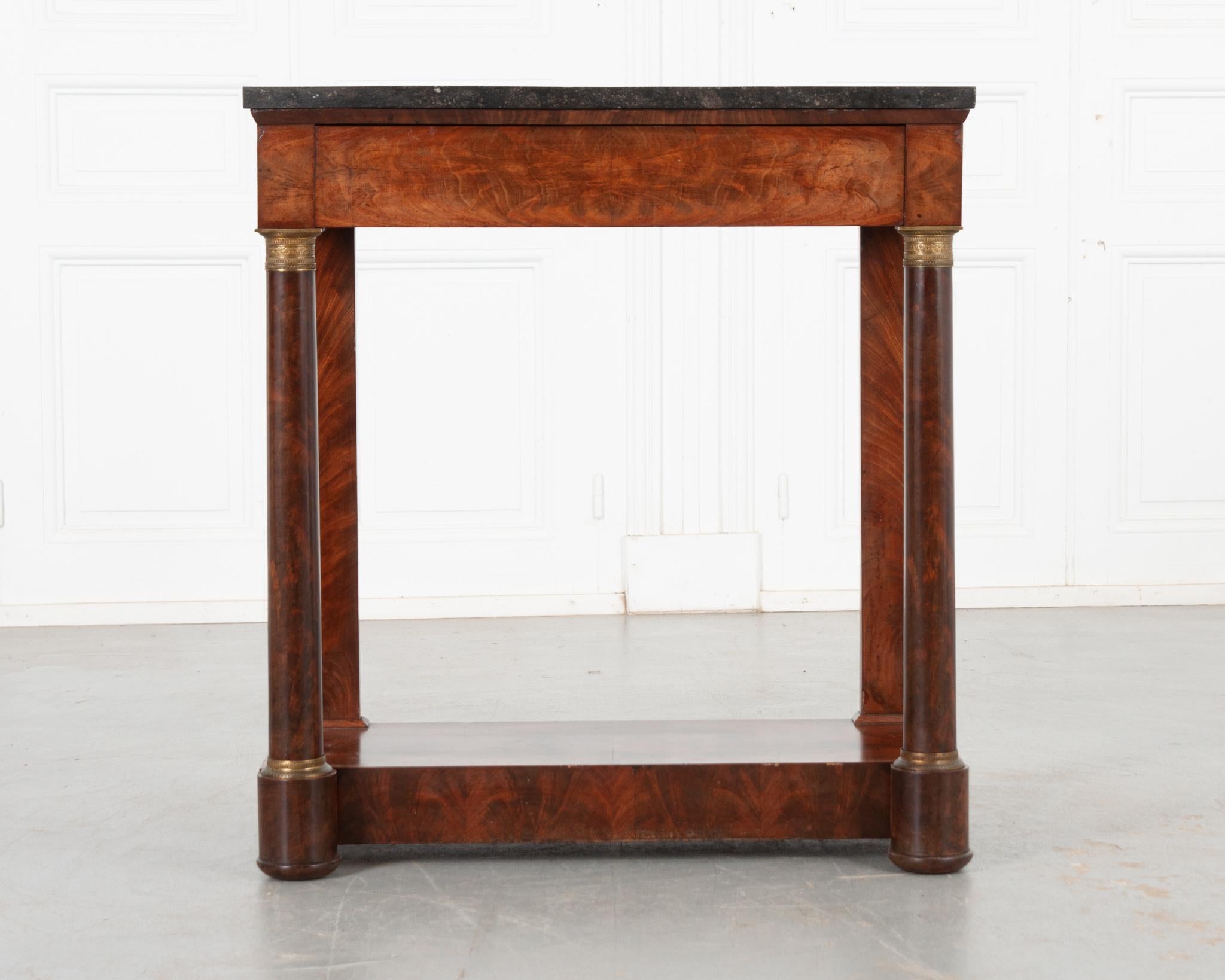 A classic and resolute French Empire console. Topped in Belgian granite, this beautiful table is finished in sensational bookmatched mahogany that is in wonderful antique condition. A single drawer is housed in the apron. Tall, column-form front