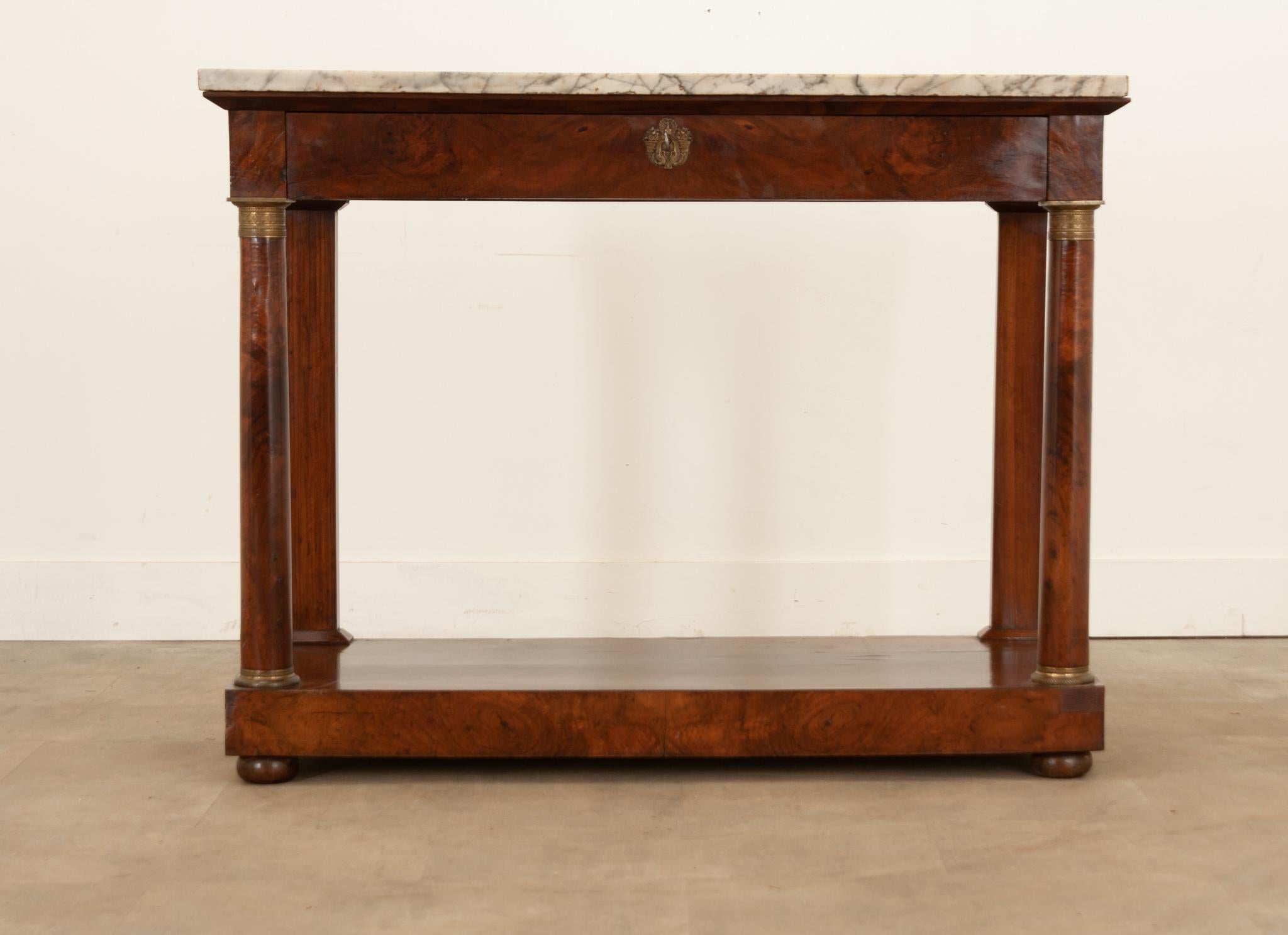 A large French Empire console, topped in marble and finished in bookmatched mahogany, made circa 1810. This Empirical antique has a white and gray marble top that is in wonderful antique condition. It has chips found about its edges and some areas