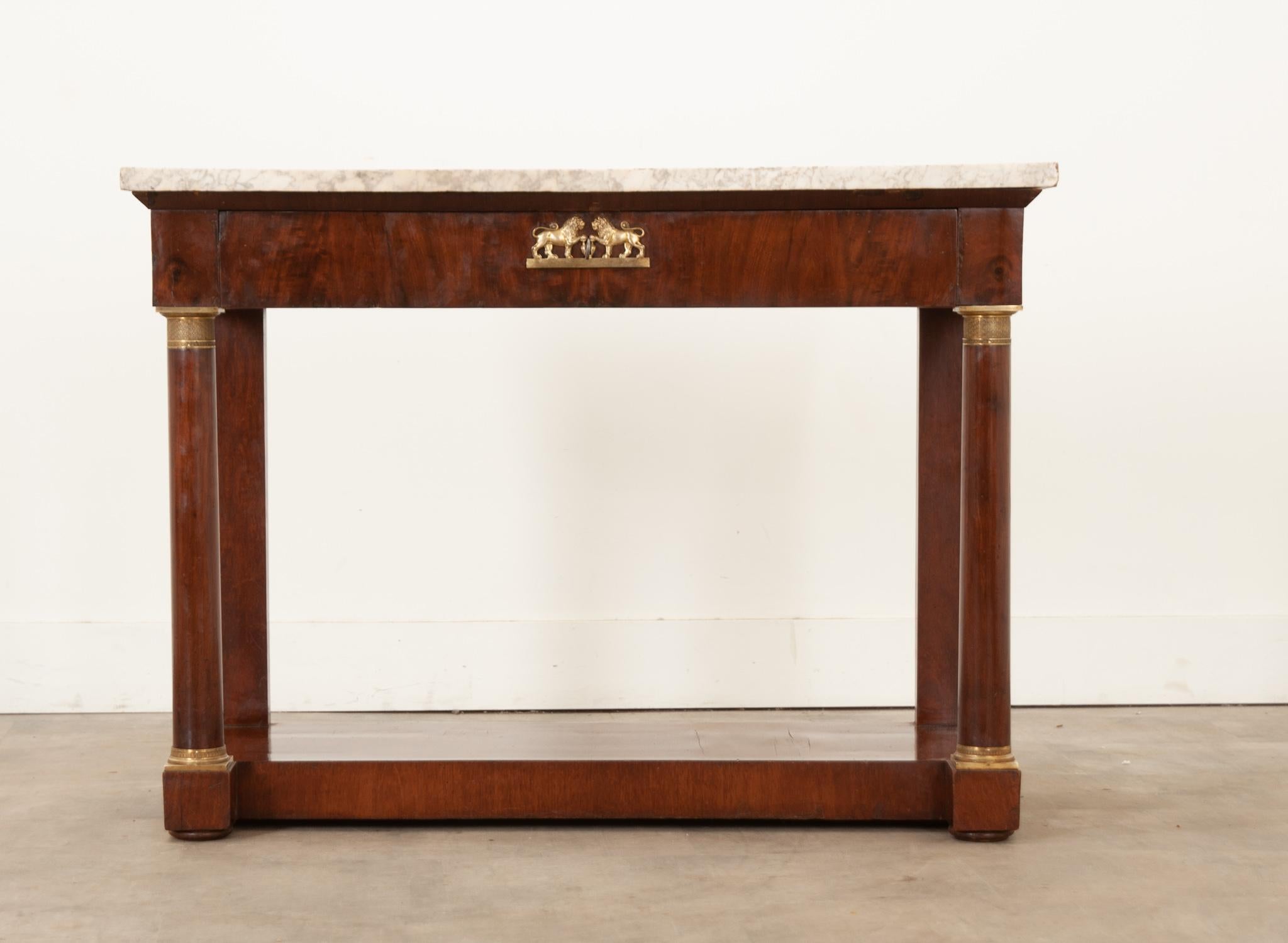 A classic French Empire console from the 19th century. Made of  warmly toned mahogany, it has gained a wonderful patina over the centuries. It retains its original white marble top with little nicks and patina, showing its age. The simple apron