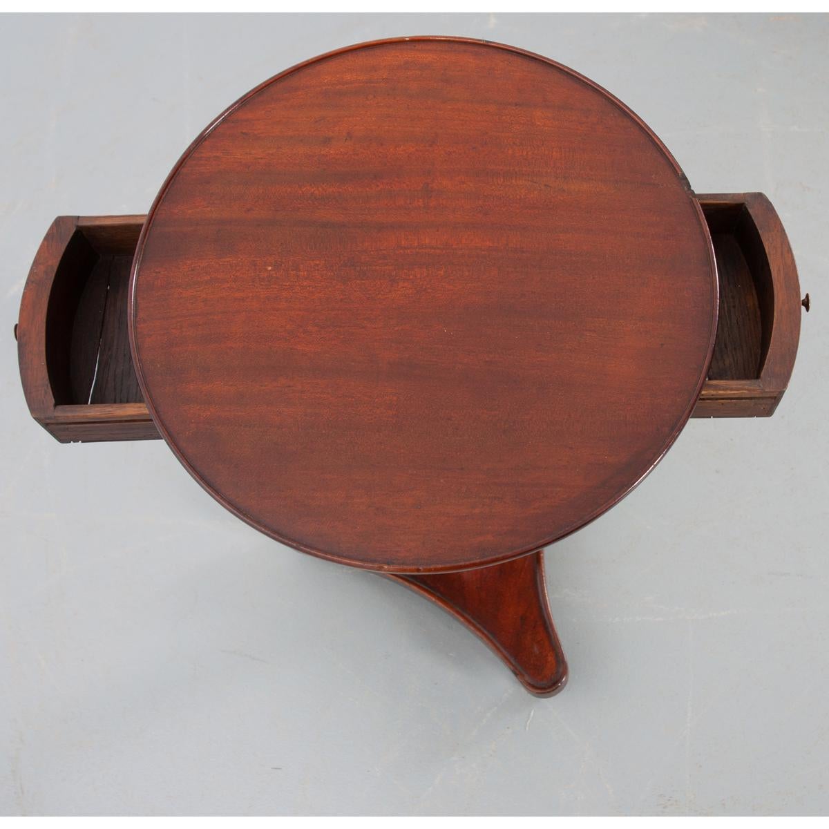 Une remarquable table d'appoint en acajou de style Empire français avec un panier unique enroulé autour du piédestal. Un plateau circulaire en bois avec une bordure en relief repose sur un tablier abritant deux petits tiroirs avec des boutons en