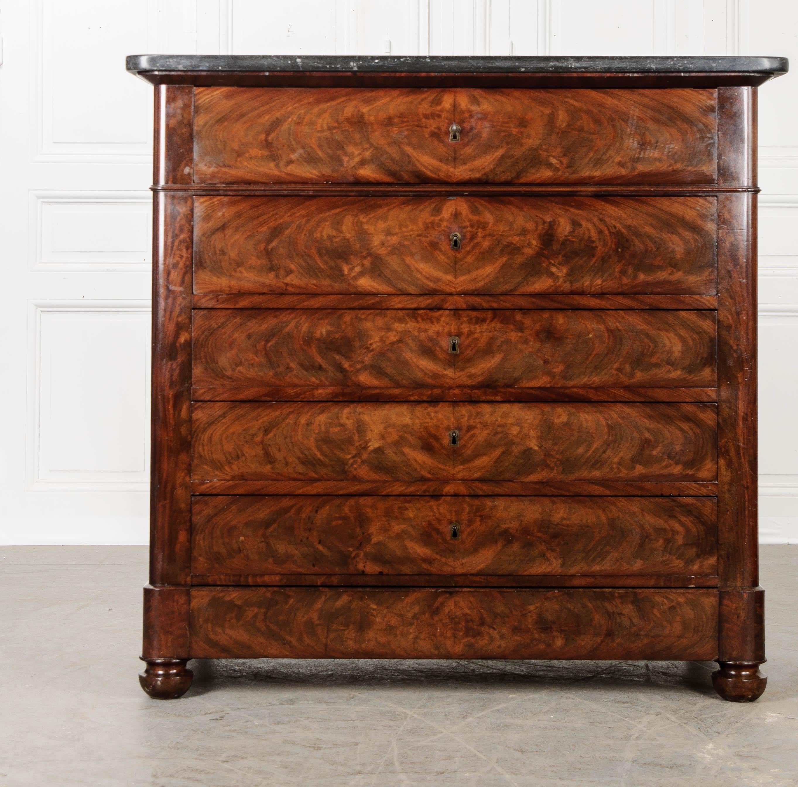 Brilliantly bookmatched mahogany graces the drawer fronts of this 19th century French commode whose resourceful design incorporates a fold out desk into one of its drawers. The case piece has six drawers in total, with the bottom-most hidden in the