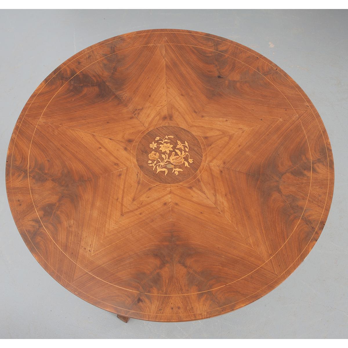 This mahogany tea table is quite nice. It has a center medallion of mixed wood inlay depicting a floral and foliate motif surrounded by two thin inlay borders. Ten book-matched and pie-shaped panels form the top around the center medallion, also