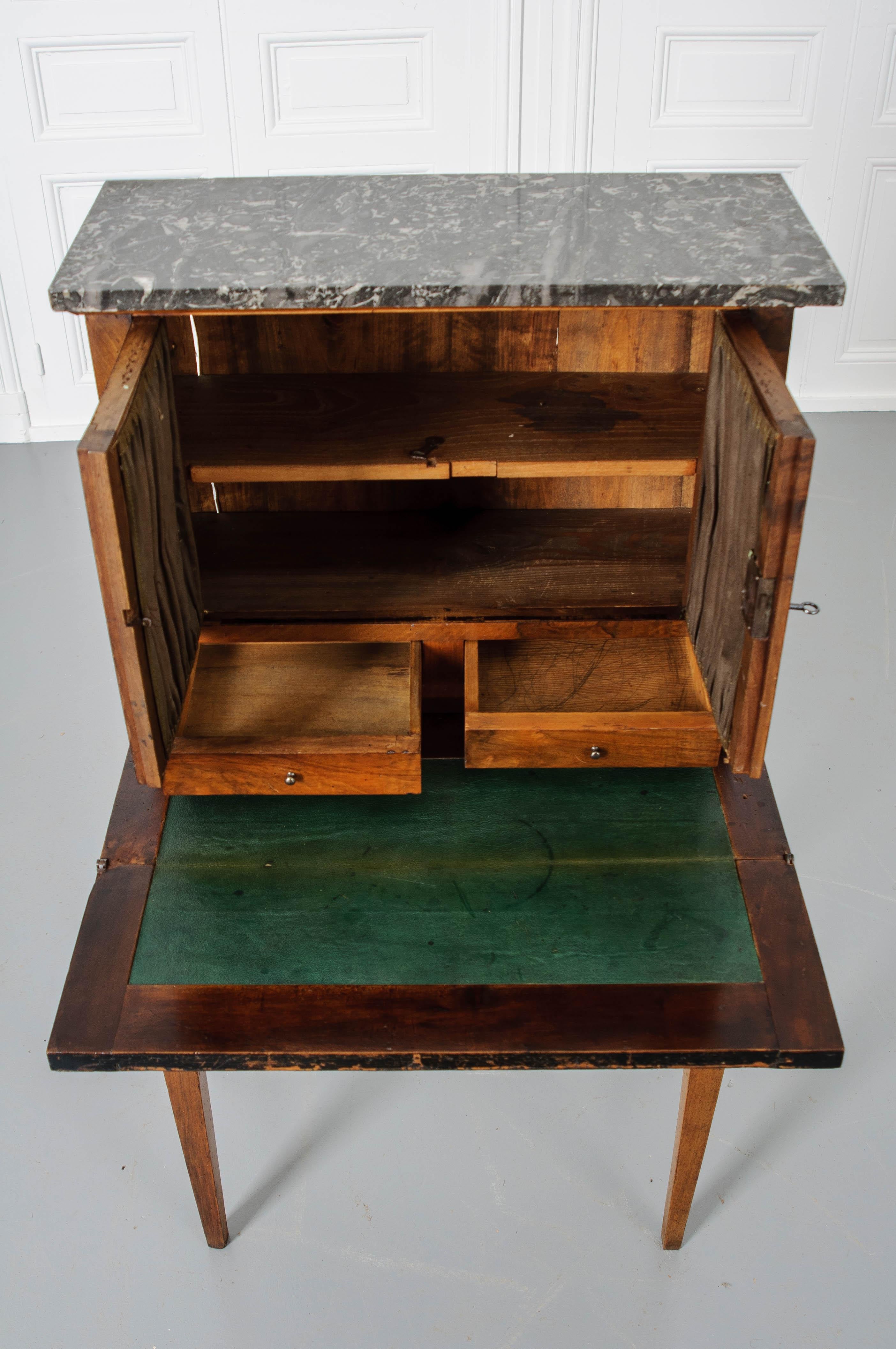 This is a charming French 19th century ladies desk. Simple details grace this desk; clean lines and antique brass hardware. A black and gray marble top sits above two glass locking doors. The doors conceal a storage space with a fixed shelf. Just