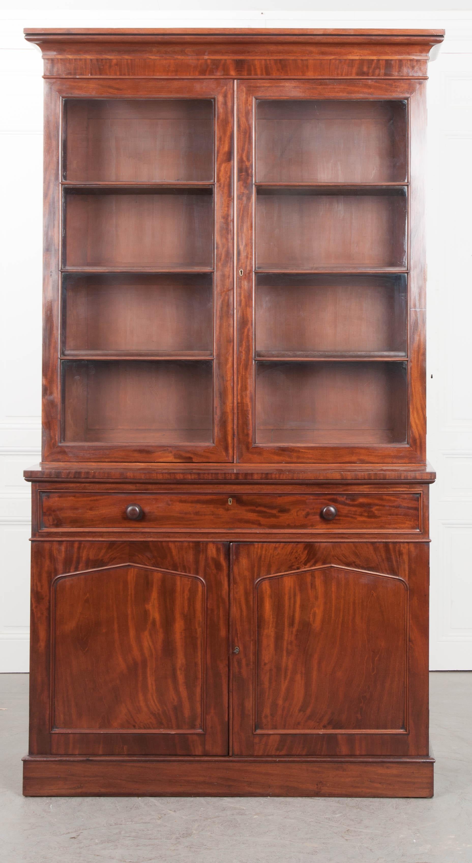 This handsome Georgian mahogany bookcase, circa 1850, would make a stunning addition to any library or den! It features a molded cornice over two glazed doors, which retain their original wavy glass, opening to a bank of four adjustable shelves. The