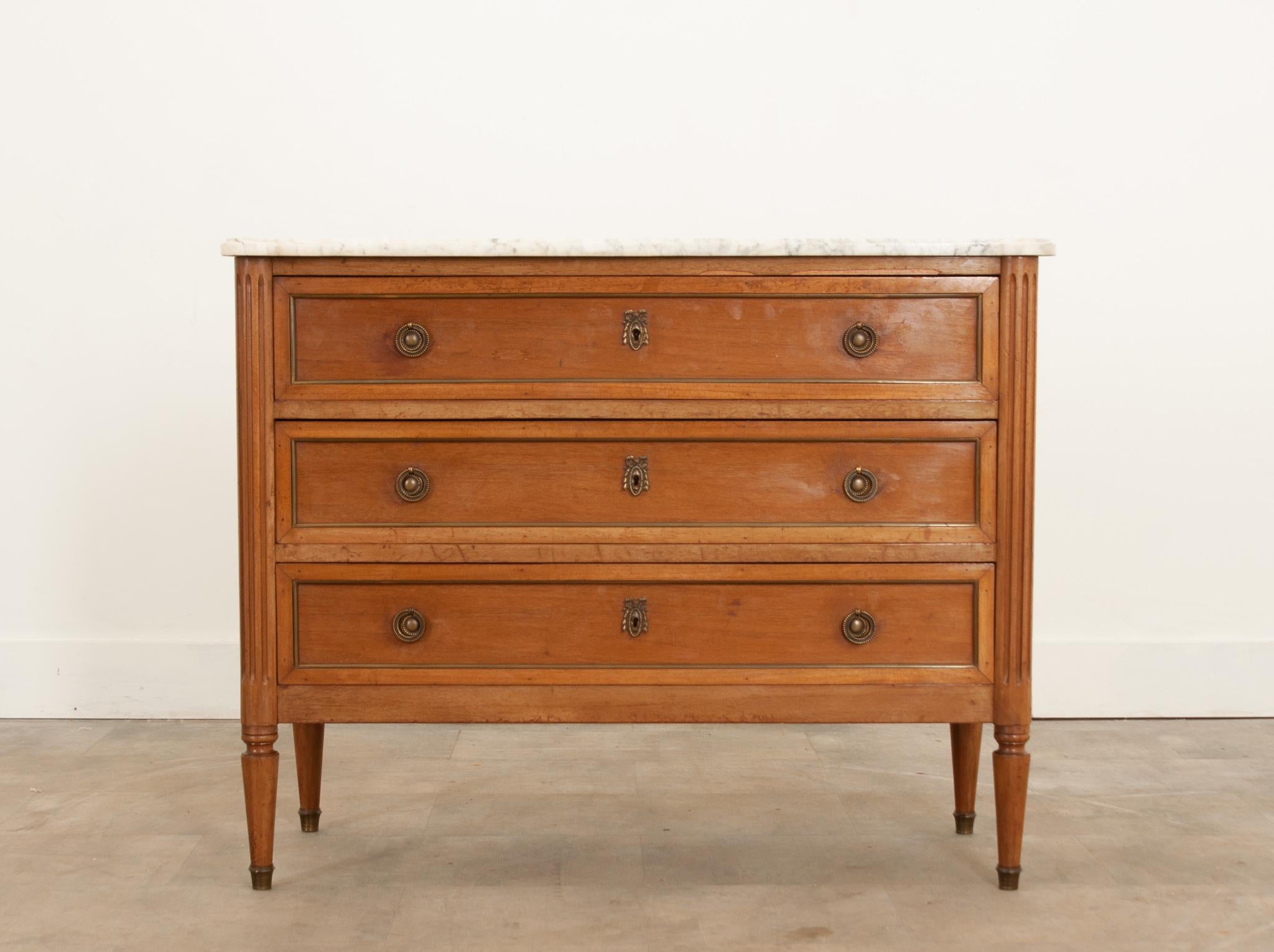 A wonderful petite mahogany, Louis XVI style commode. Its original shaped marble top is in good antique condition and has a molded edge. A bank of three drawers each have brass banding, a pair of decorative drop ring pulls, and laurel swag